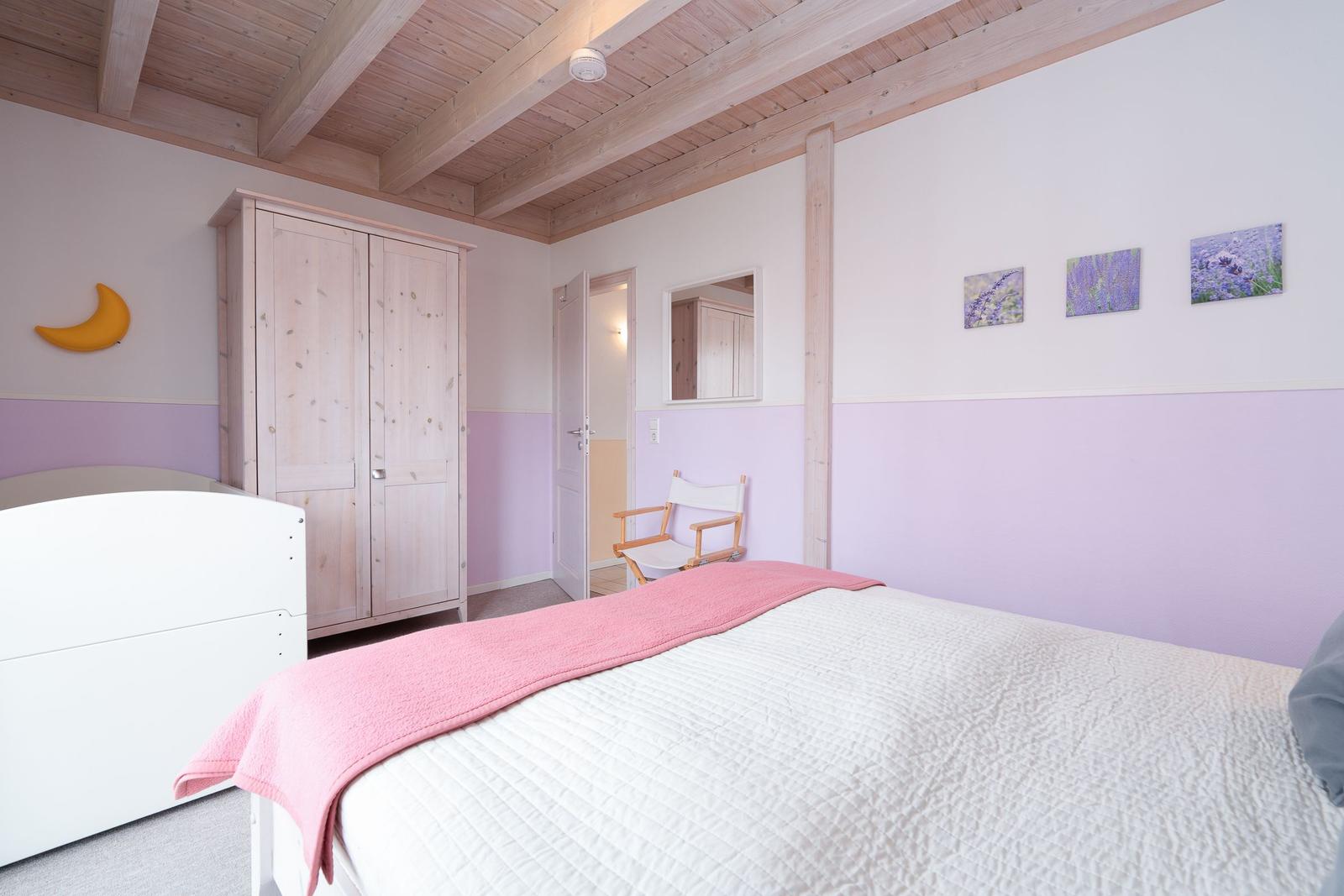 Schlafzimmer mit Bett, Kleiderschrank und Wandbildern.