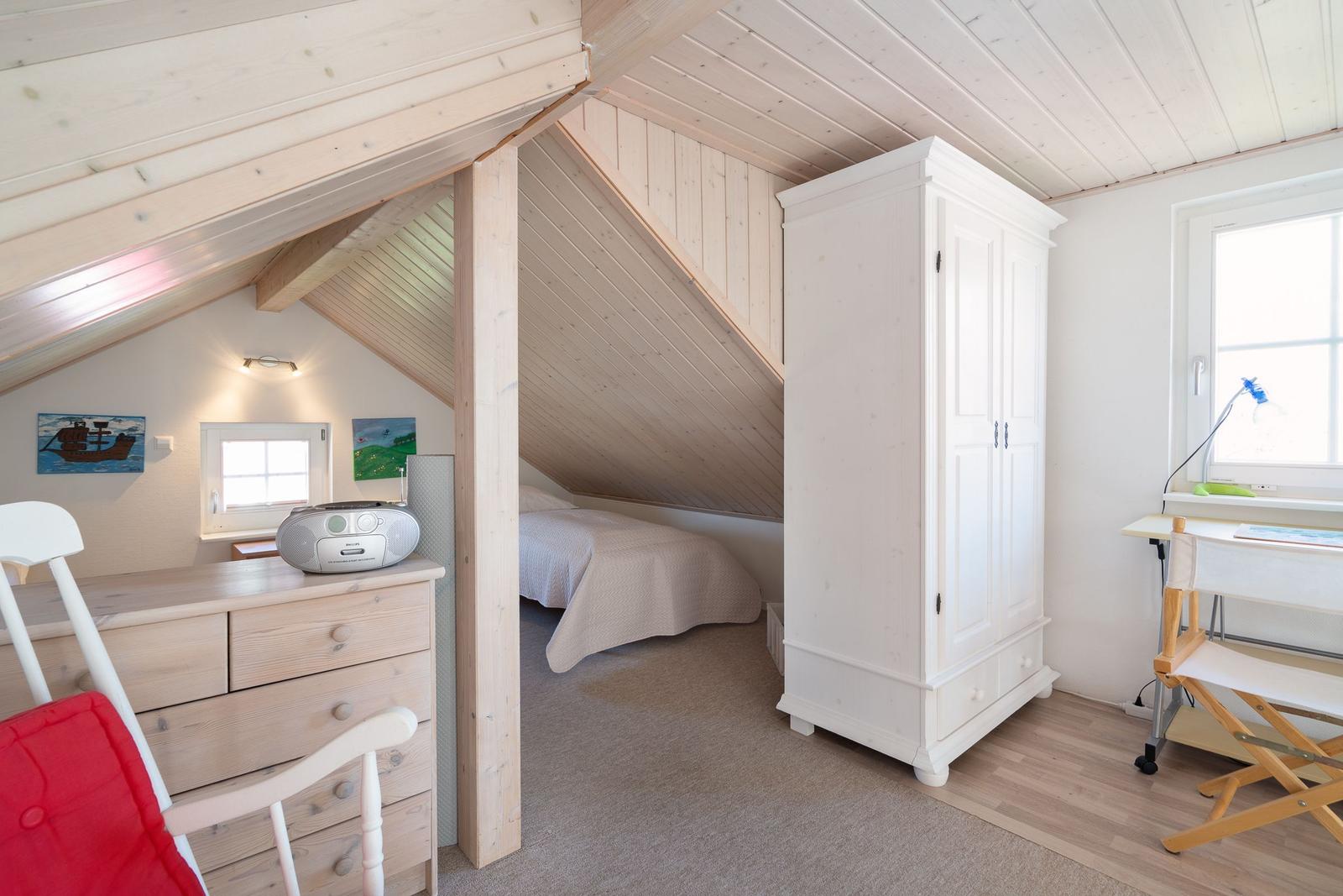 Schlafzimmer mit Dachschräge, weißem Schrank und Schreibtisch mit Stuhl.