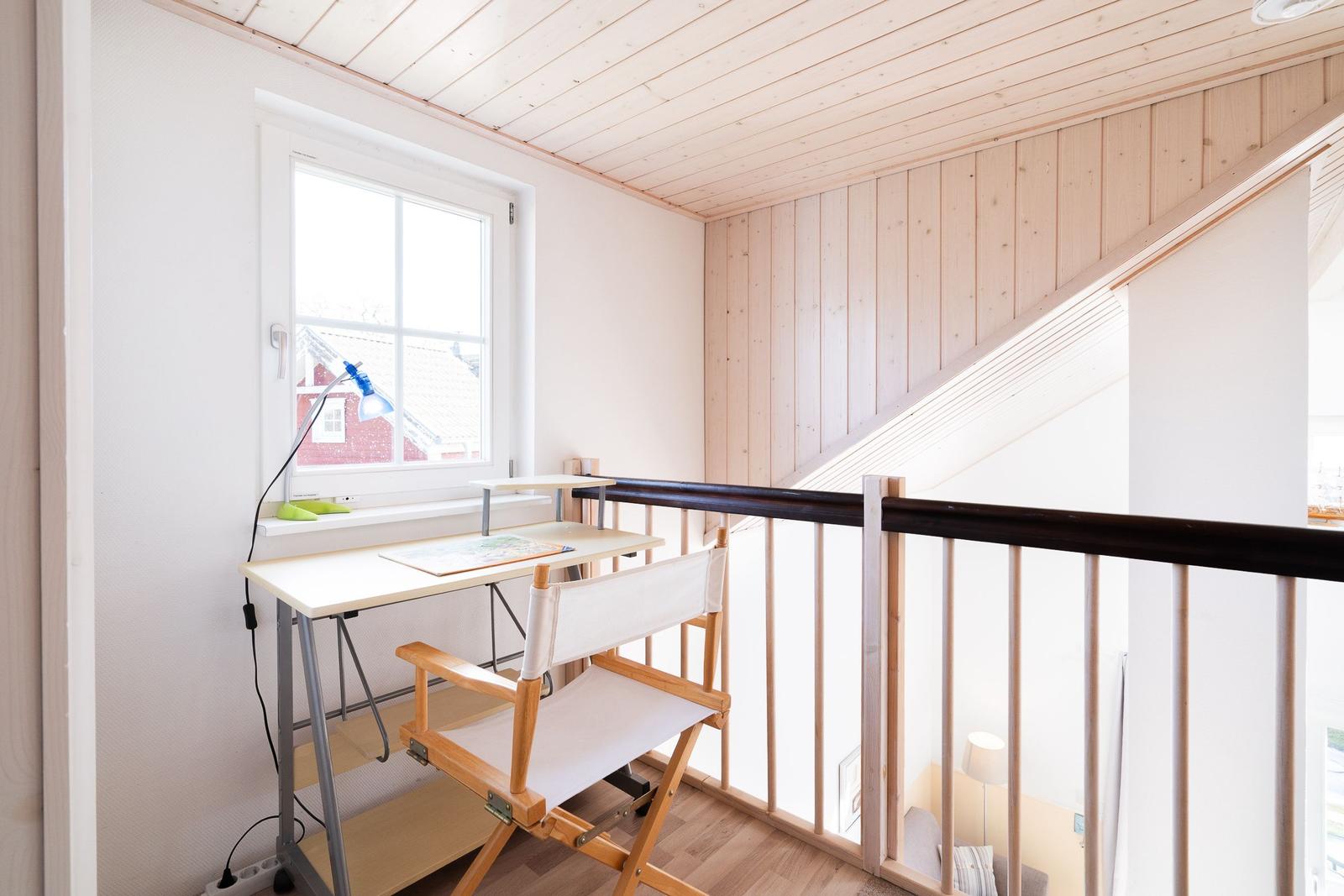 Arbeitsplatz mit Schreibtisch und Stuhl unter einem Fenster mit Blick nach draußen.