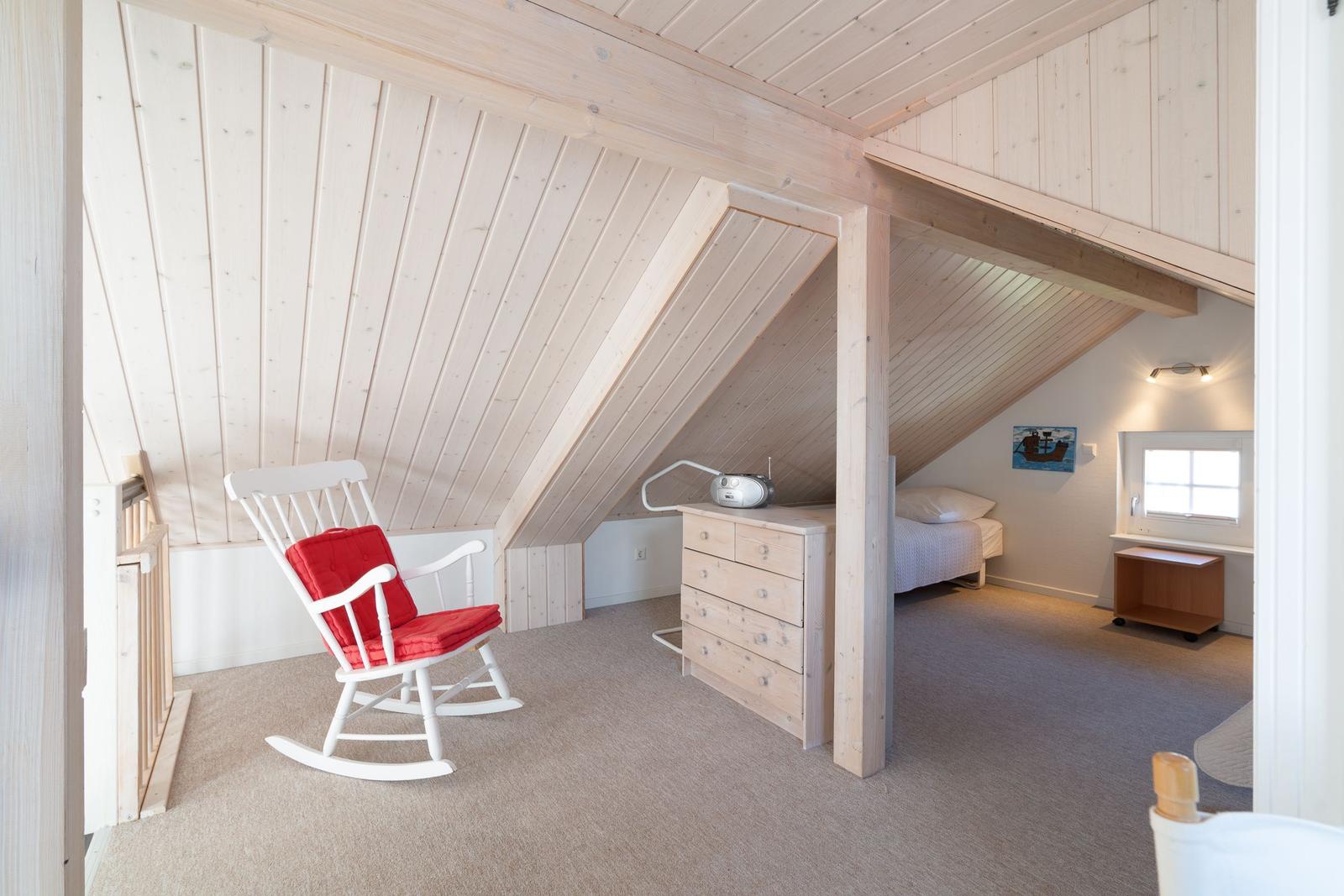 Schlafzimmer mit weißem Schaukelstuhl und rotem Sitzkissen. Holzdecke und -wände.