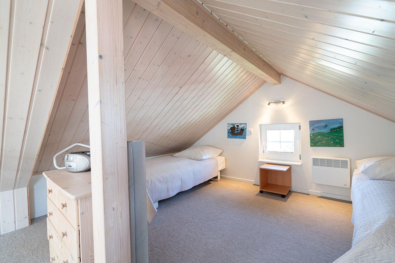 Schlafzimmer mit zwei Betten, Holzdecke und Fenster. Möbel und Bilder sind sichtbar.