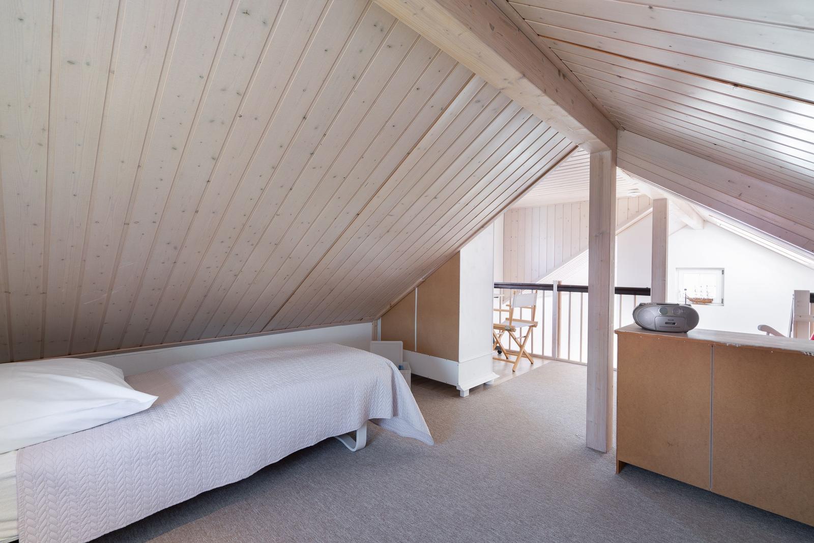 Schlafzimmer mit Dachschrägen, Bett, Schrank und Blick auf Balkon.