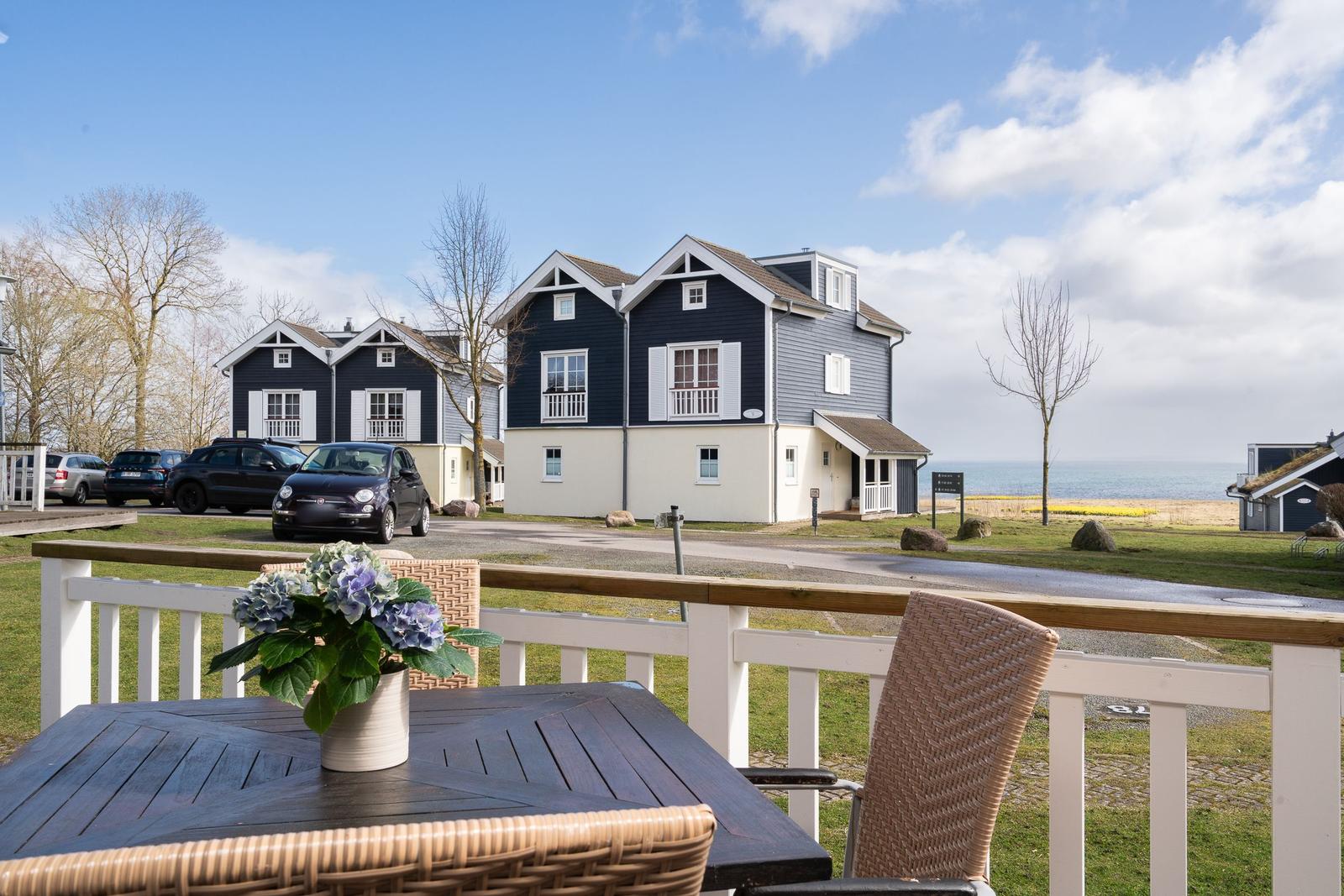 Terrasse mit Tisch und Stühlen. Im Hintergrund stehen Häuser und das Meer.