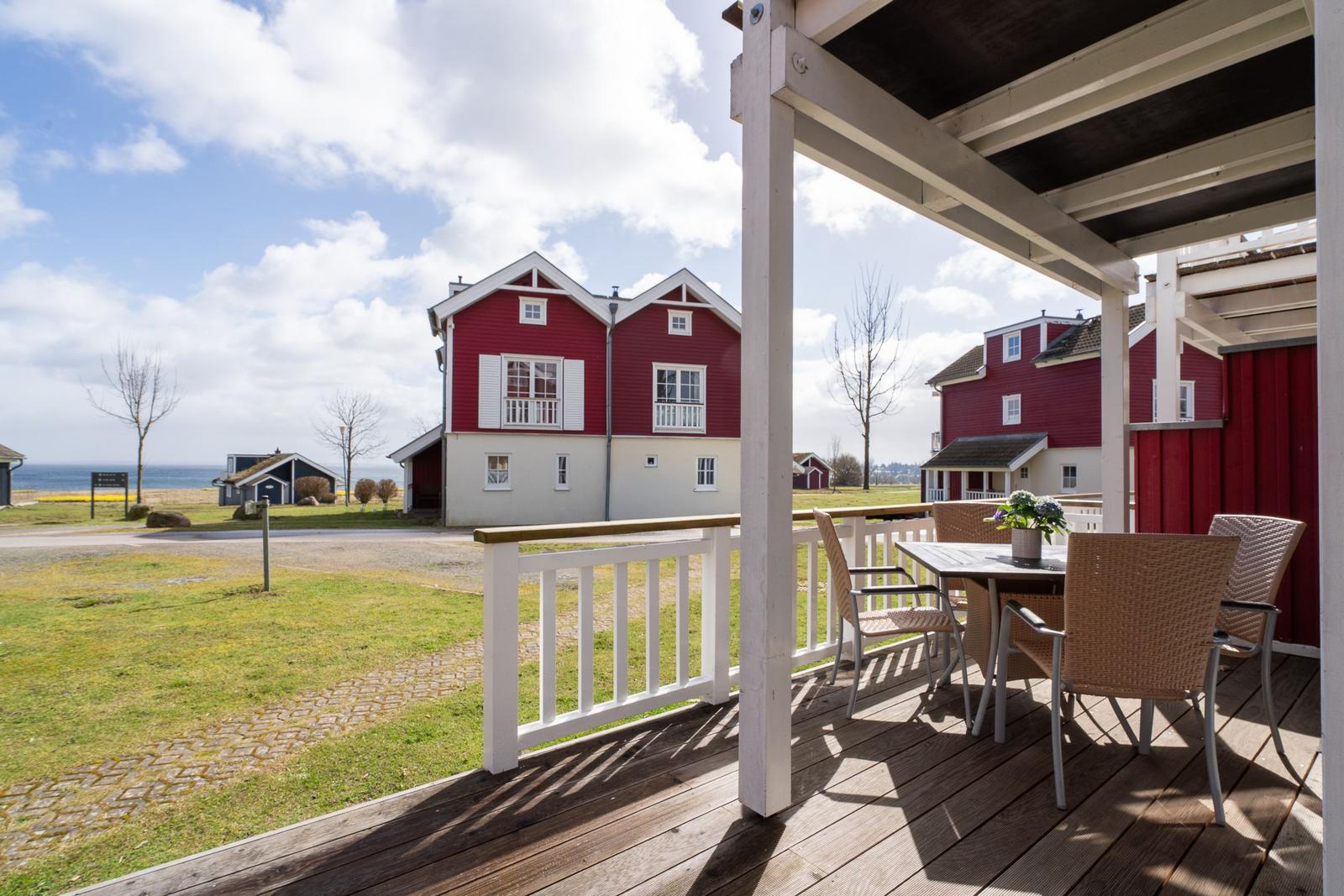 Terrasse mit Tisch und Stühlen. Roter Holzaufbau mit Blick auf Küstenhaus.