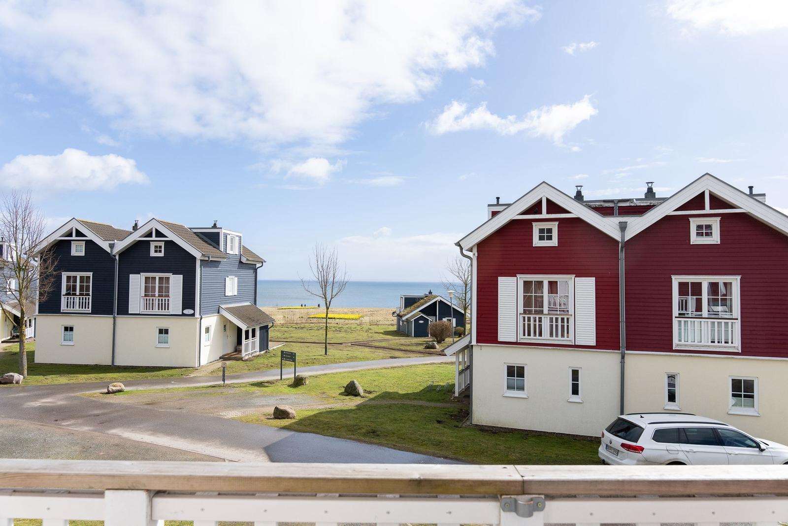 Zwei Häuser mit Blick aufs Meer, rotes und blaues, mit Balkonen und Grünfläche.