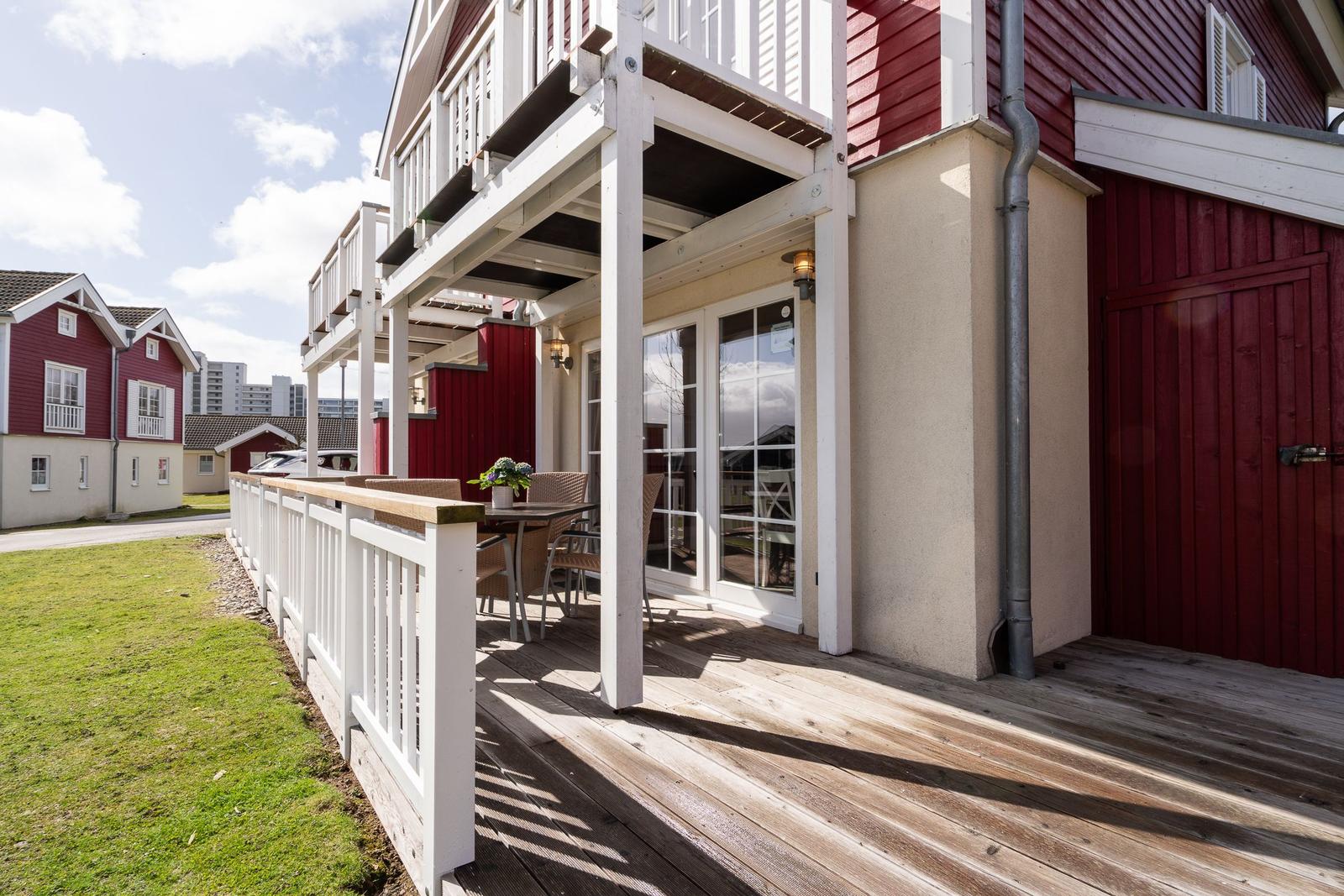 Terrasse mit Tisch und Stühlen vor einem roten Haus mit weißem Geländer.