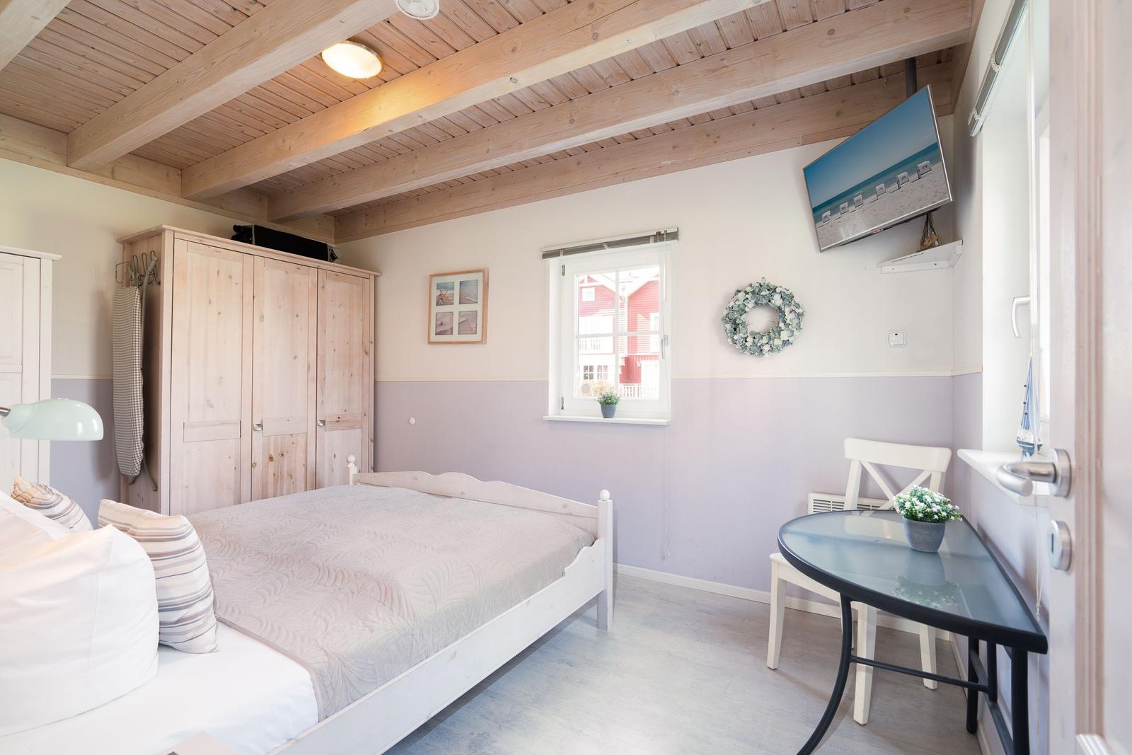 Schlafzimmer mit Bett, Kleiderschrank, Tisch und Fernseher an der Wand.