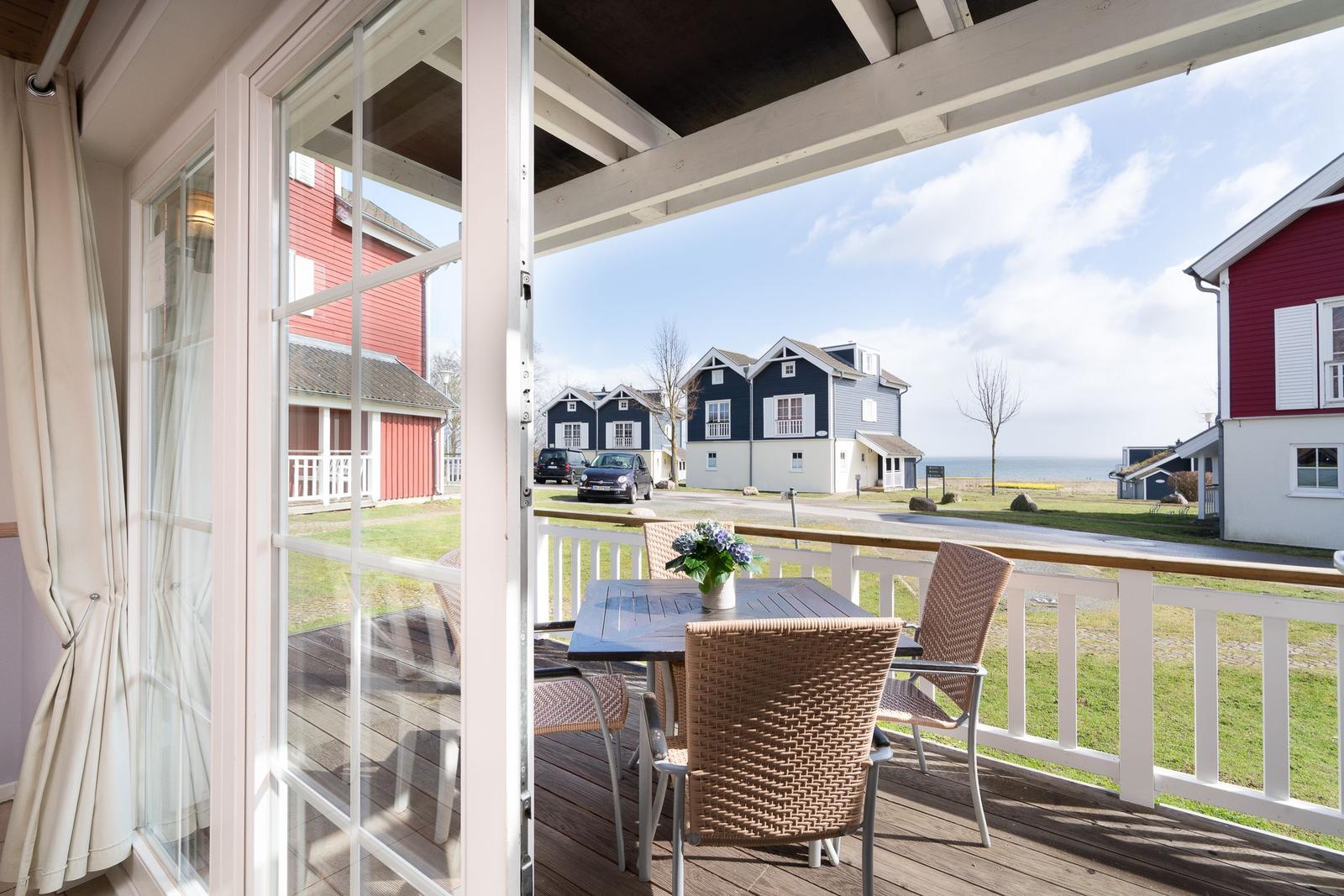 Terrasse mit Tisch und Stühlen. Blick auf rote und blaue Häuser und das Meer.