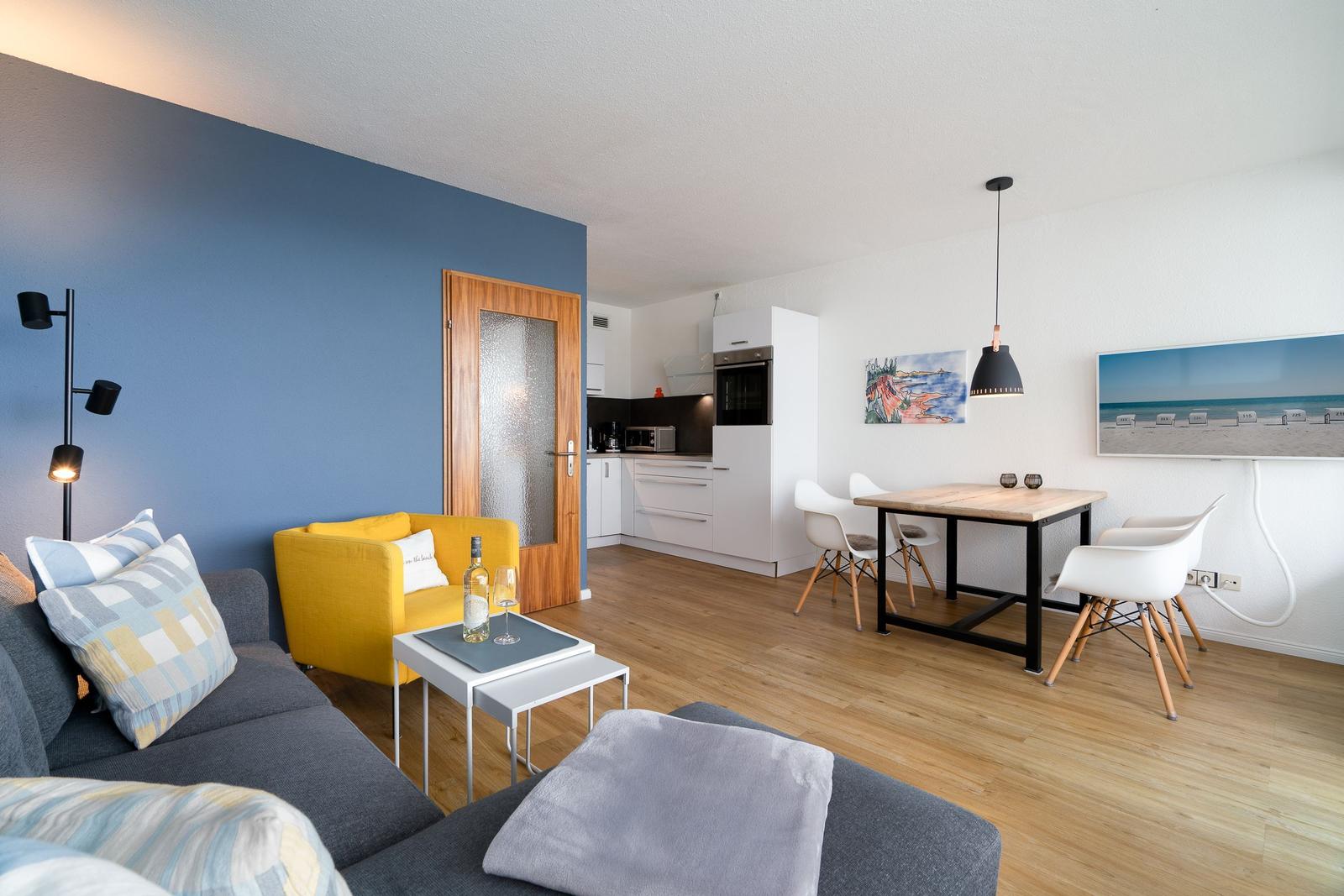 Wohn- und Essbereich mit Küchenzeile, Sofa, Sessel und Esstisch mit Stühlen.