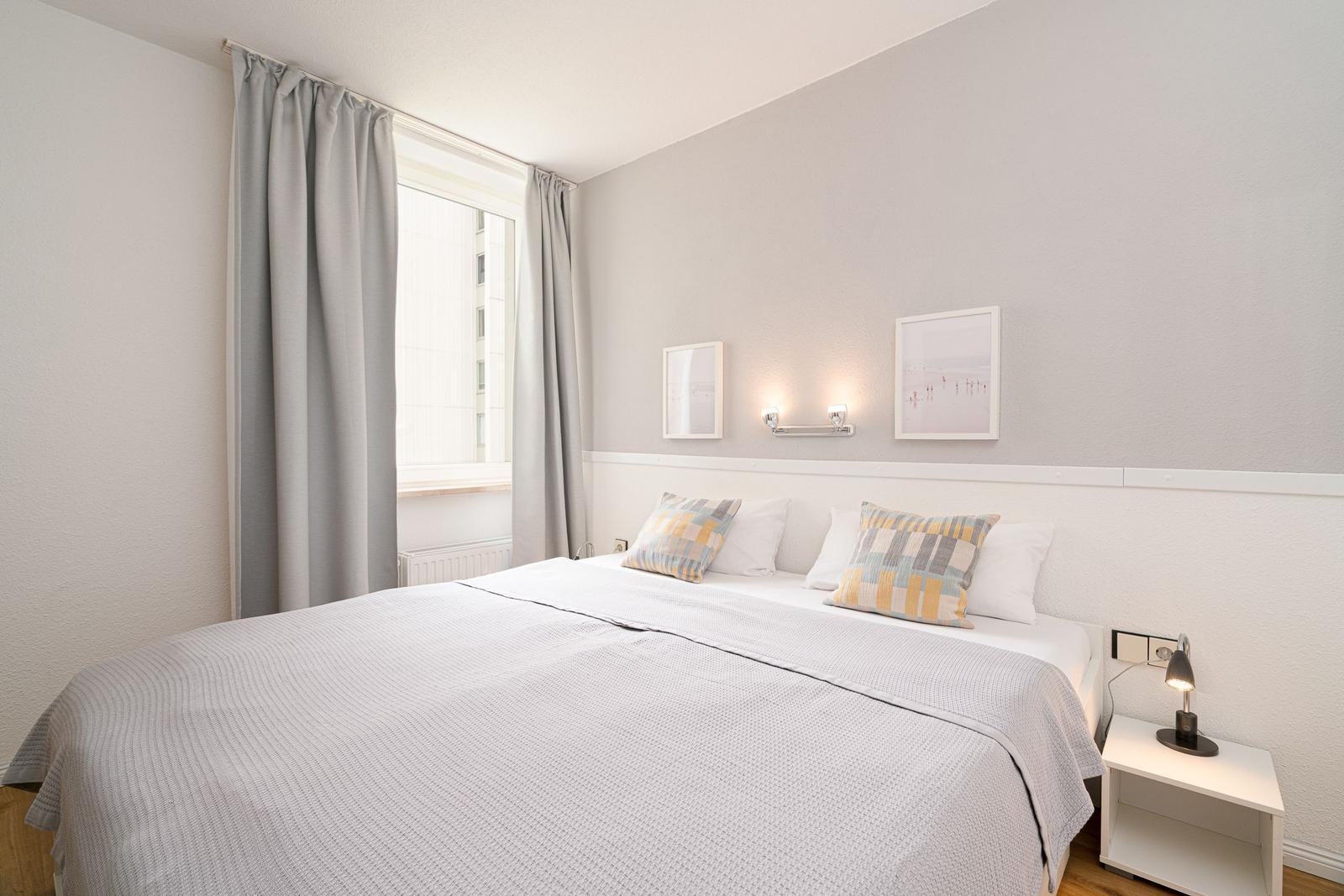 Schlafzimmer mit Doppelbett, Fenster und Nachttisch mit Lampe.
