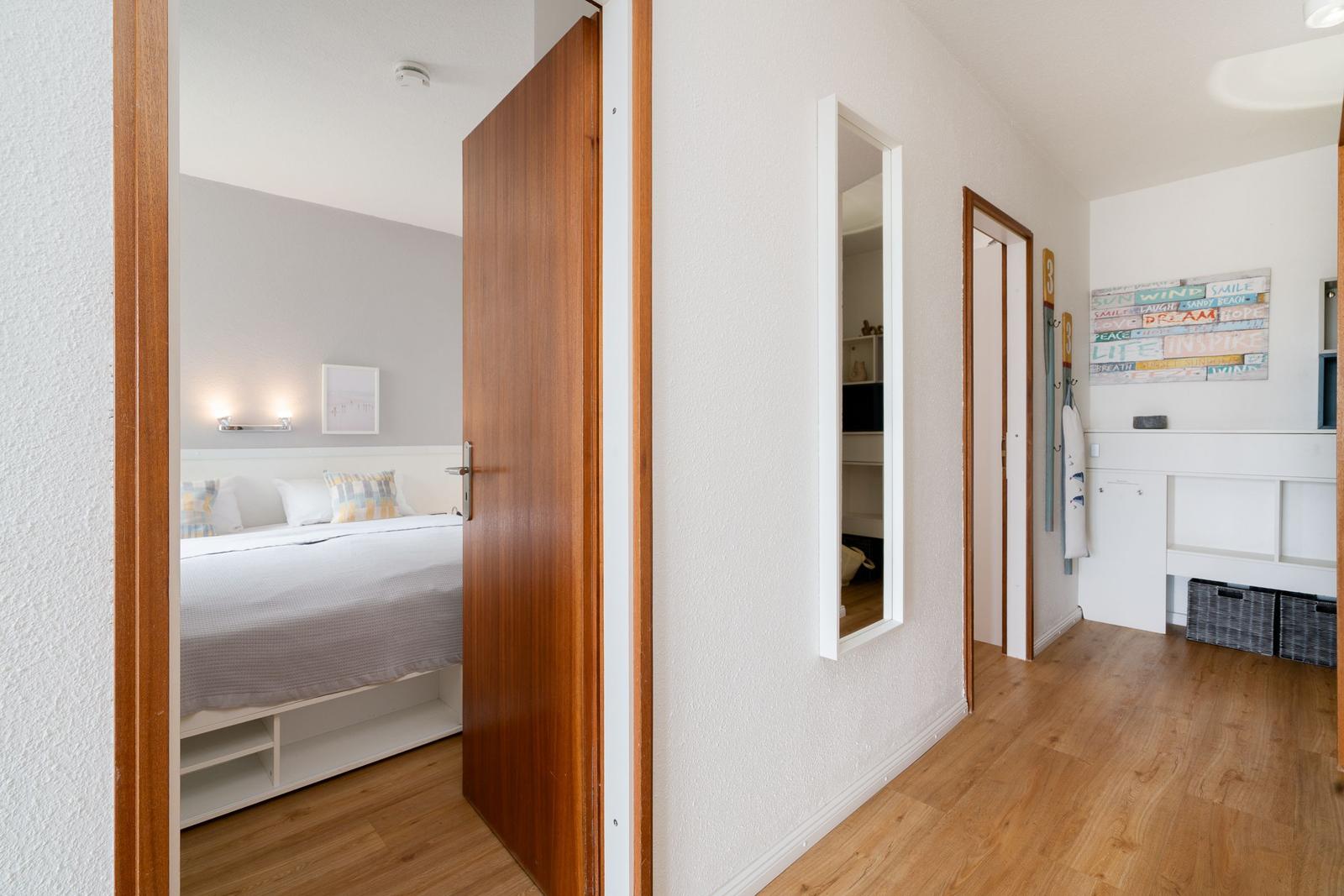 Schlafzimmer mit Bett und Wandbild. Flur mit Spiegel und Kleiderständer.