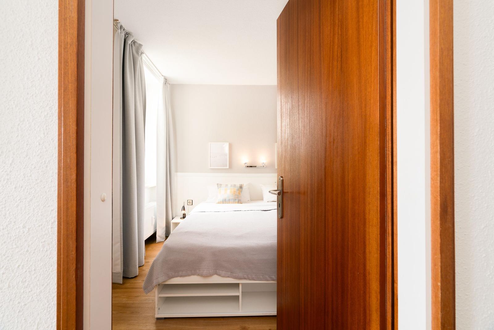 Schlafzimmer mit Bett, Nachttisch und Fenster mit Vorhängen.