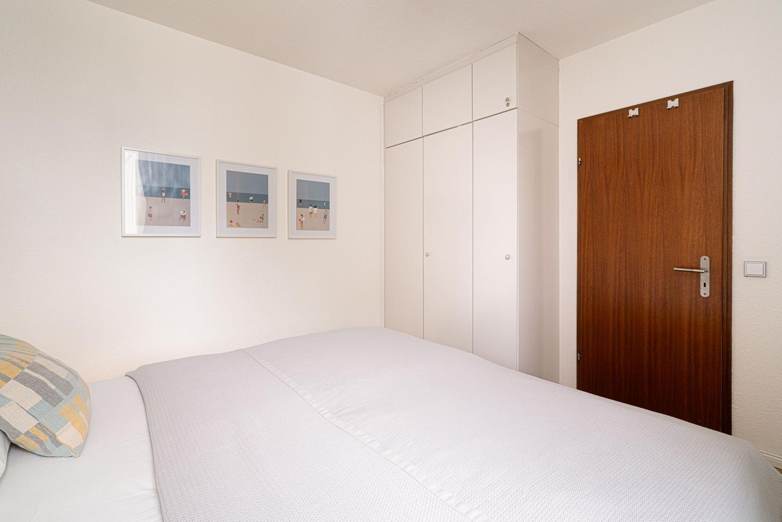 Schlafzimmer mit Bett, Kleiderschrank und Tür. An der Wand hängen drei Bilder.