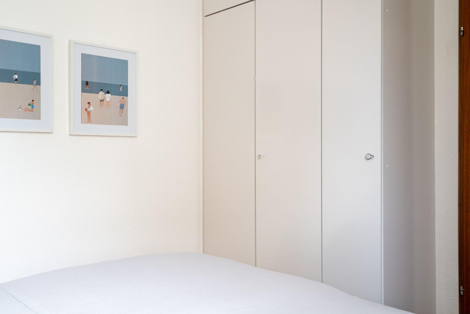 Schlafzimmer mit Bett, Kleiderschrank und zwei Bildern an der Wand.