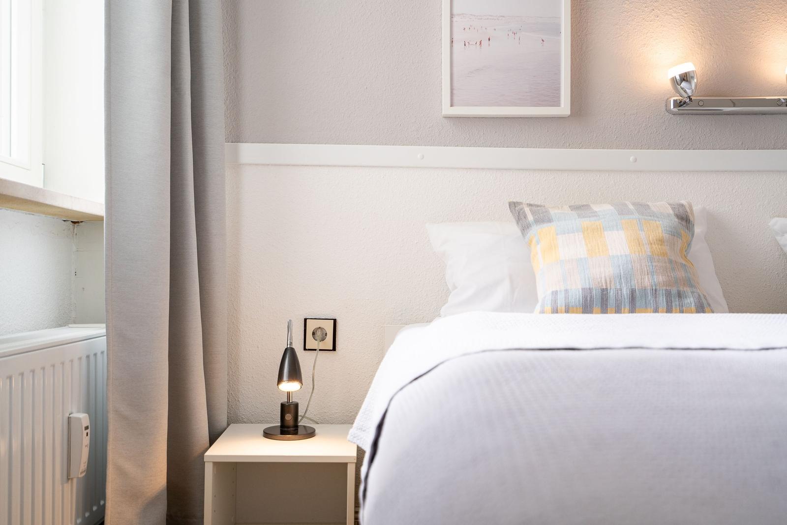 Schlafzimmer mit Bett, Nachttisch, Lampe und Wandbild.