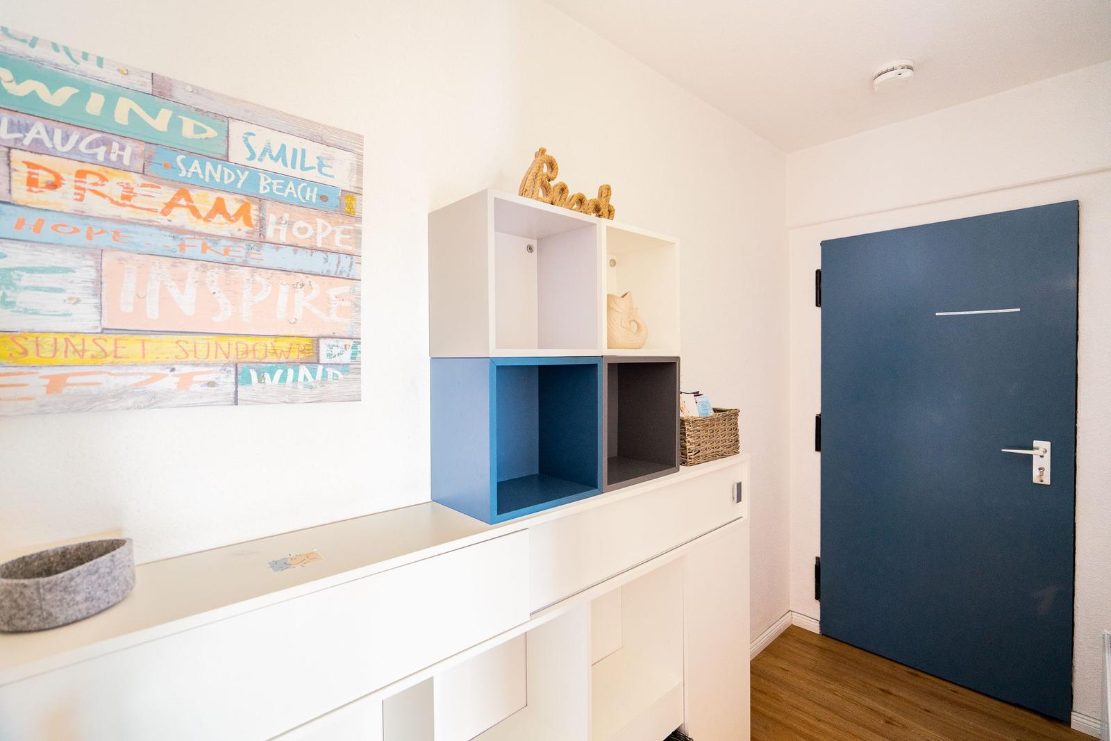 Eingangsbereich mit blauer Tür, weißen Schränken und Wandbild mit Motiven.