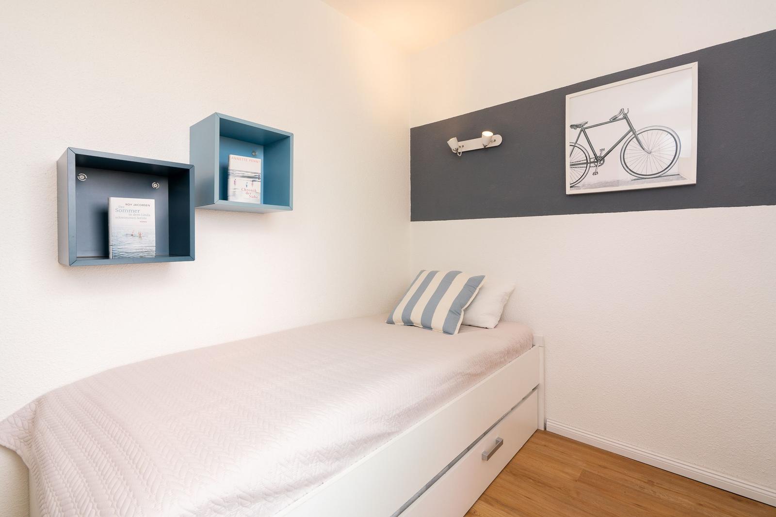 Ein Schlafzimmer mit Einzelbett, Wandregalen und Fahrradbild.