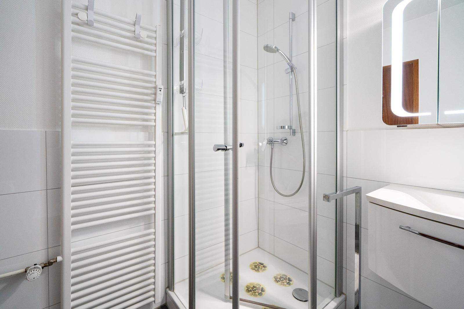 Dusche mit Glaswand, Heizkörper und Waschtisch mit beleuchtetem Spiegel.