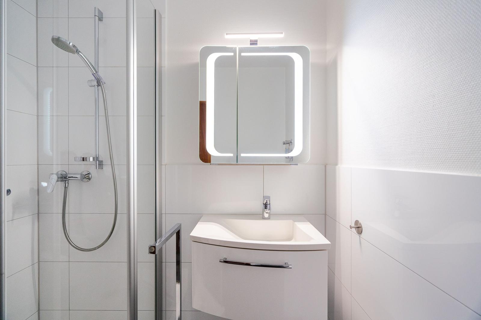 Badezimmer mit Dusche, Waschbecken und beleuchtetem Spiegel.