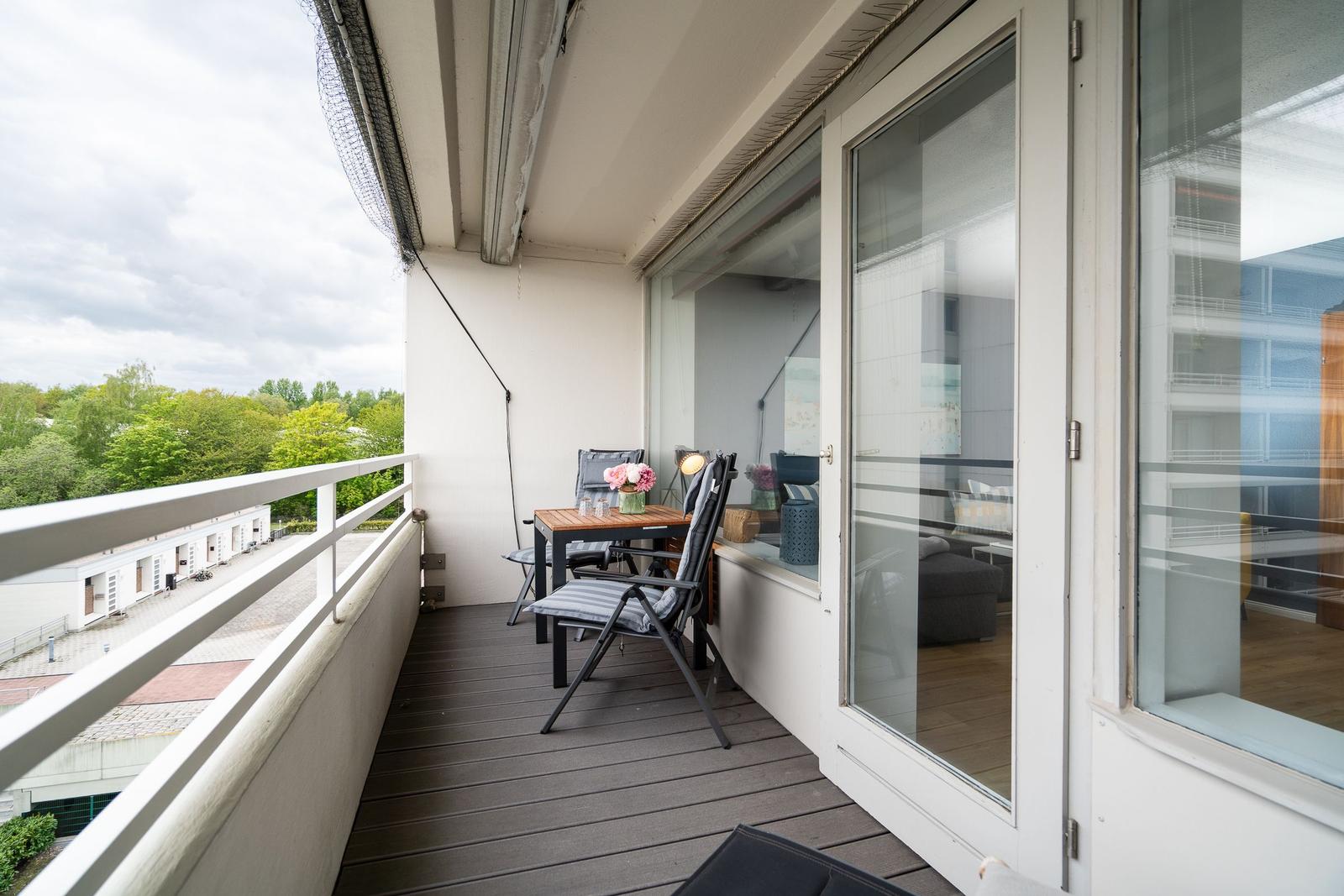 Terrasse mit Tisch, Stühlen und Blick auf grüne Bäume.