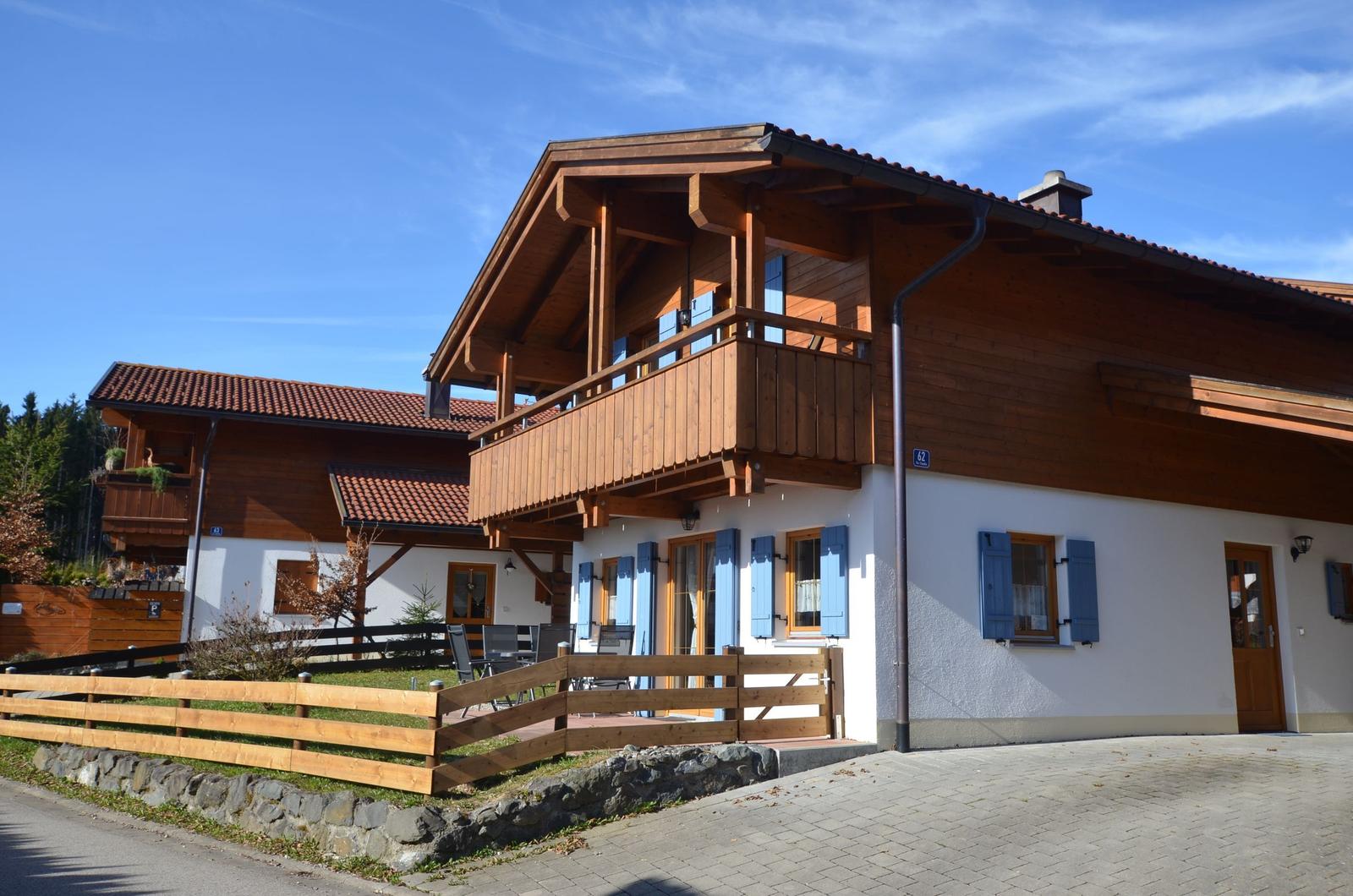 Wooden house with balcony, blue shutters, and garden area
