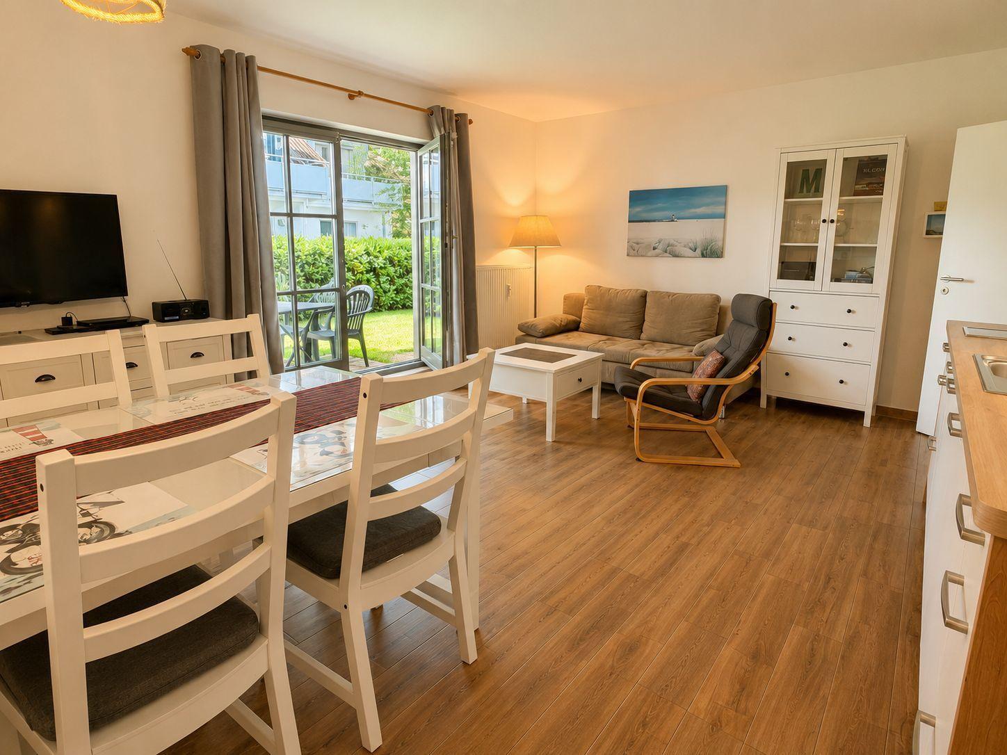 Wohn- und Essbereich mit Holzboden, Sofa, Stühlen und Blick auf die Terrasse.