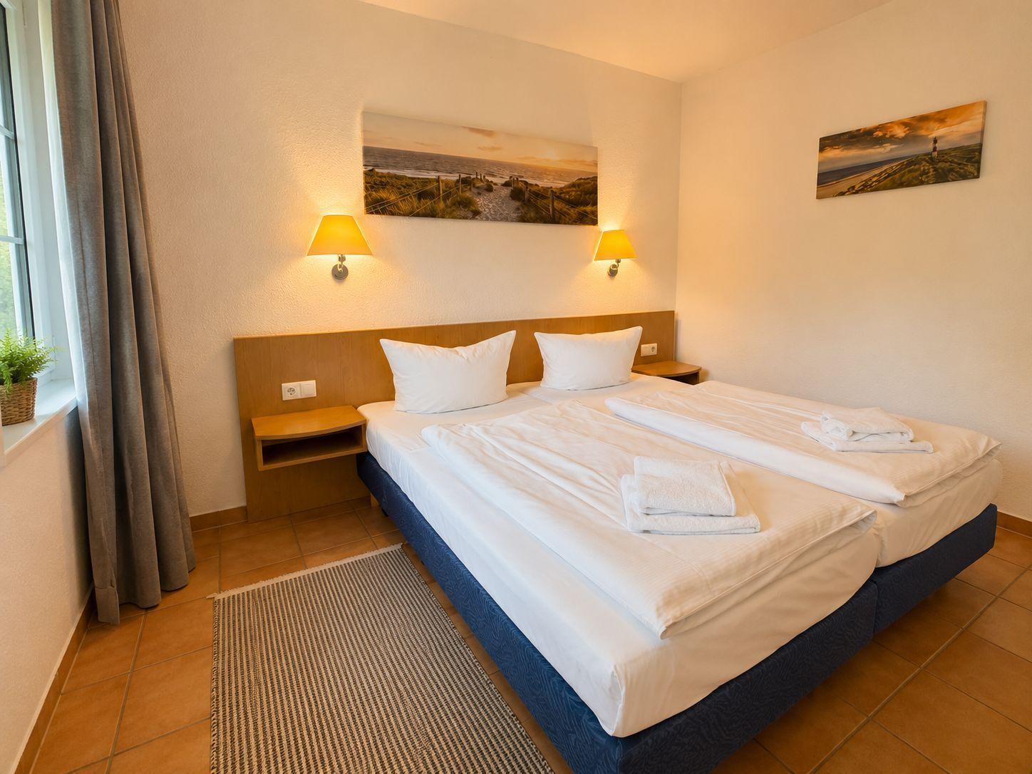 Schlafzimmer mit Doppelbett, zwei Nachttischen und Wandbildern an der Wand.