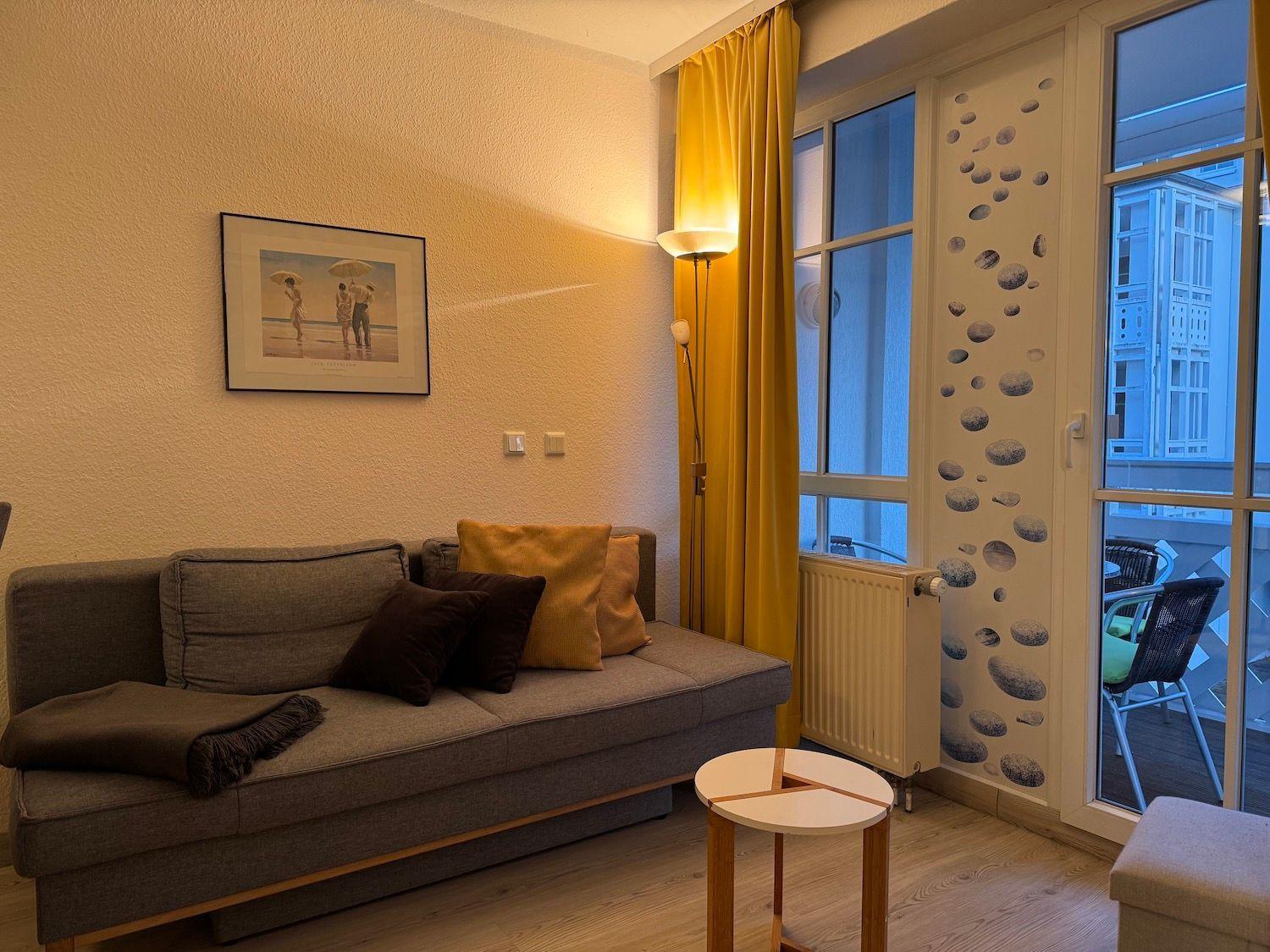 Living room with sofa, cushions, table, and view onto balcony with seating.
