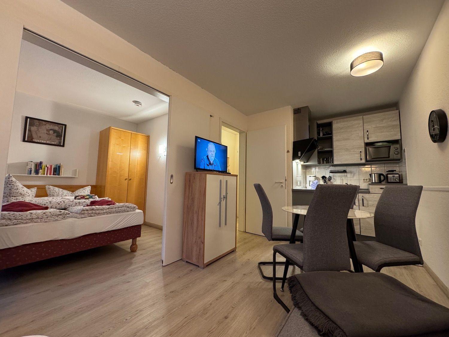 Apartment with bedroom, dining area, and kitchen. TV, cabinet, and table with chairs visible.