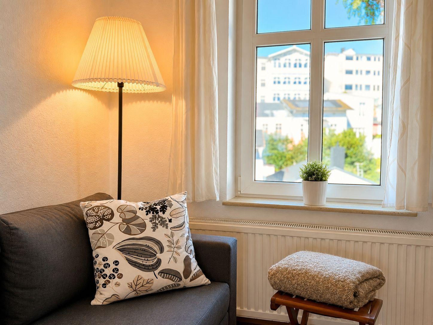 Ein grauer Sitzplatz mit Kissen, Stehlampe und Blick auf Gebäude.