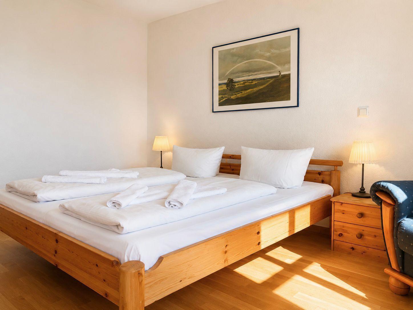 Ein Schlafzimmer mit Holzbett, weißen Bettwäsche und Nachttischen mit Lampen.