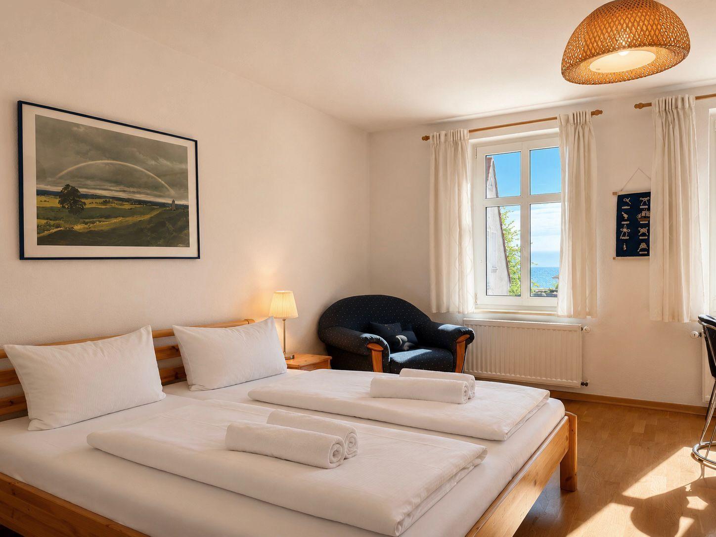 Schlafzimmer mit Doppelbett, Sessel und Fensterblick auf Meer.