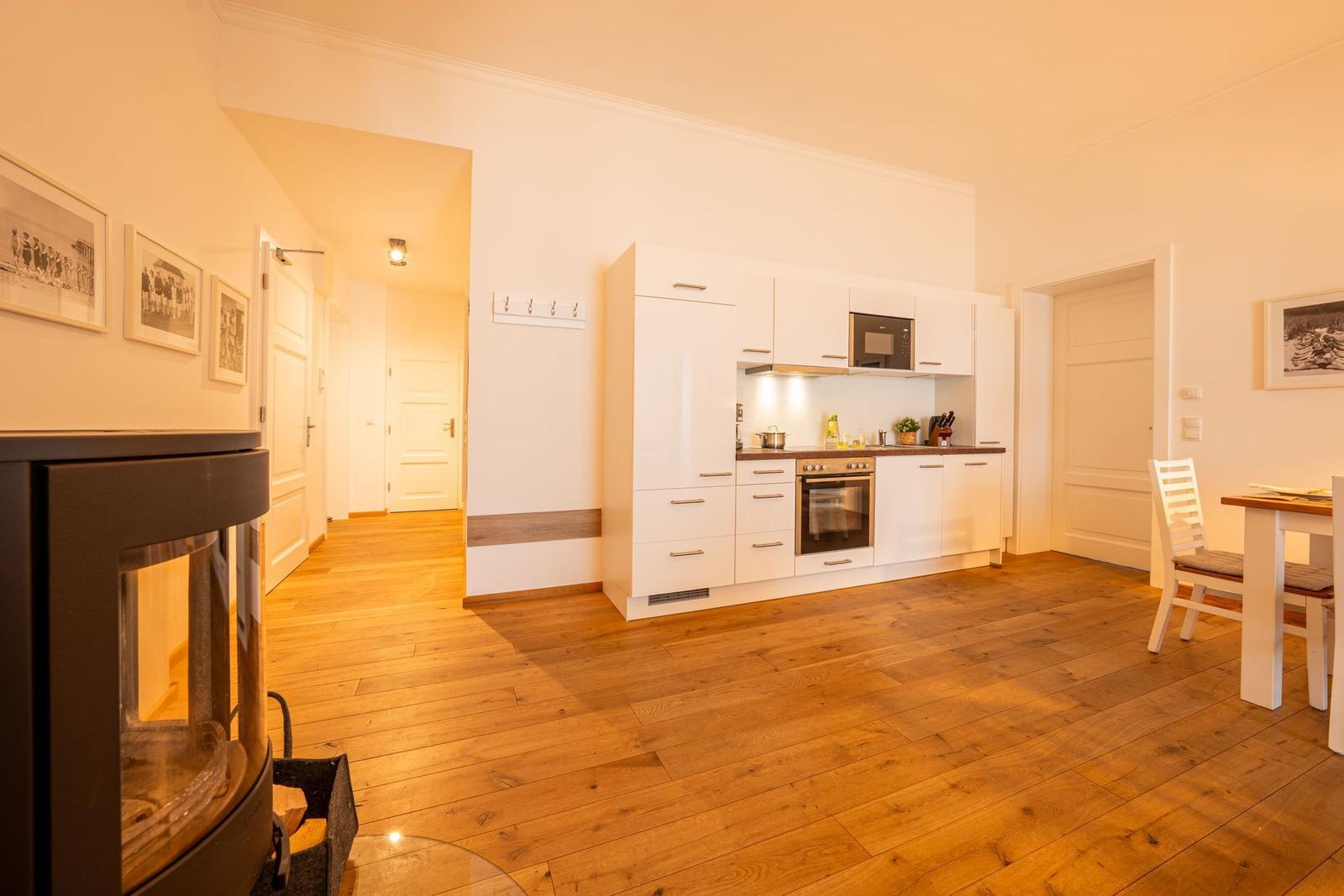 Küche mit weißen Schränken und Holzboden. Esstisch mit Stuhl. Kamin im Vordergrund.