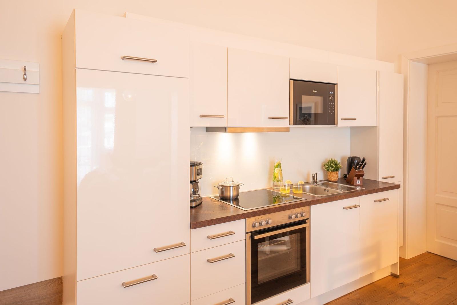 Moderne Küche mit weißen Schränken, Dunstabzugshaube und Edelstahlgeräten.