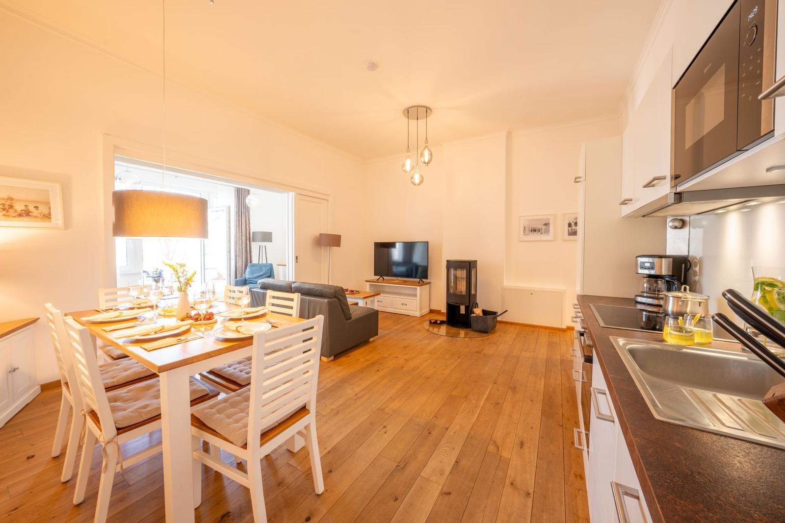 Essbereich mit Tisch und Stühlen, Küche mit Arbeitsplatte und Mikrowelle, Wohnbereich mit Sofa und Fernseher.