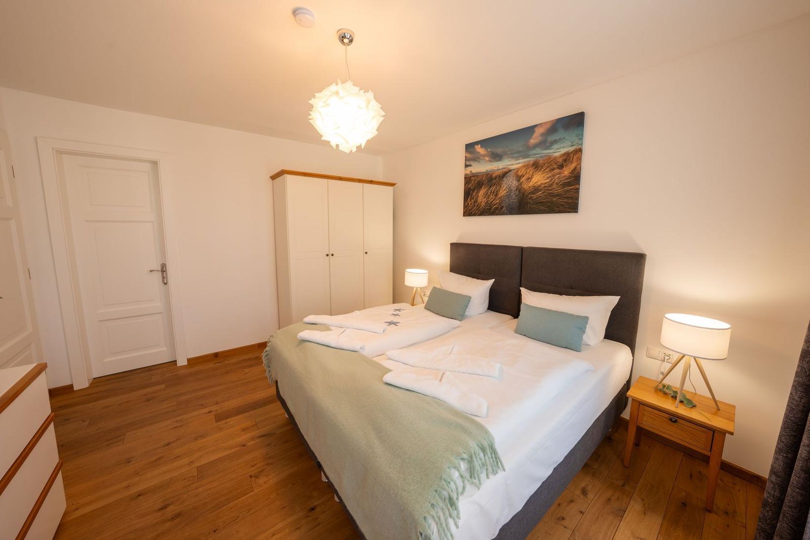 Schlafzimmer mit Doppelbett, Kleiderschrank und Nachttisch. Holzfußboden und Wandbild.