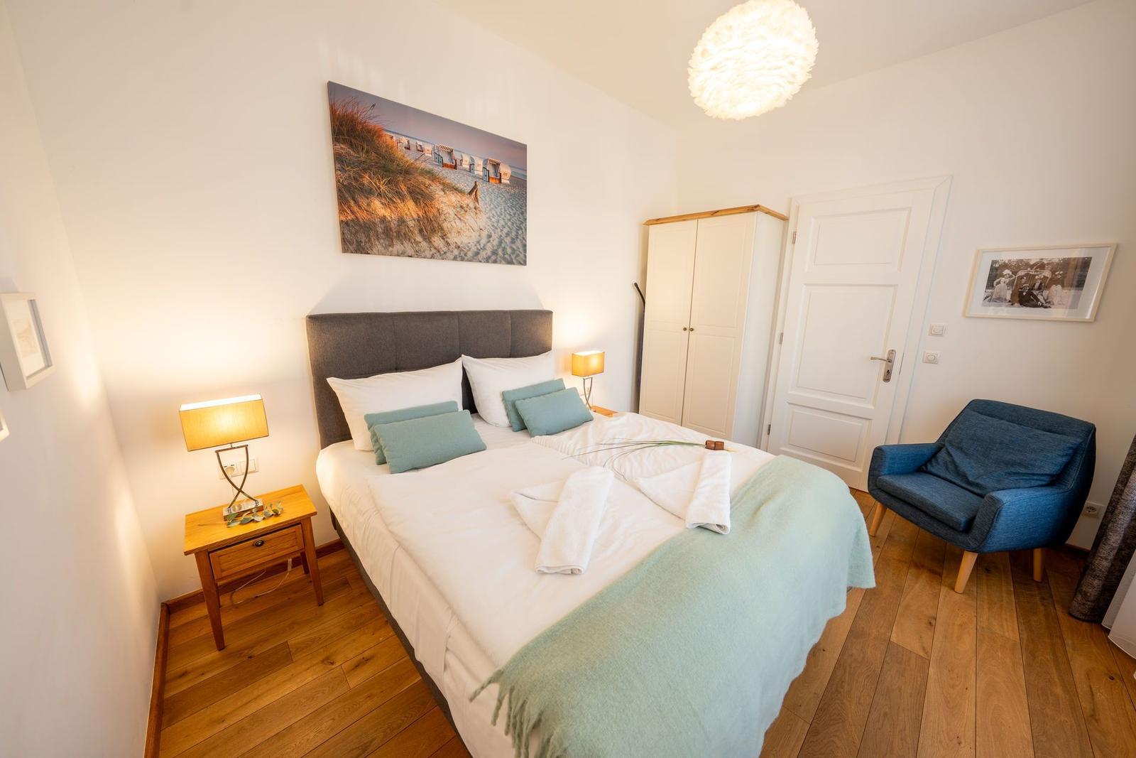 Schlafzimmer mit Doppelbett, Nachttisch, Stuhl und Wandbild.