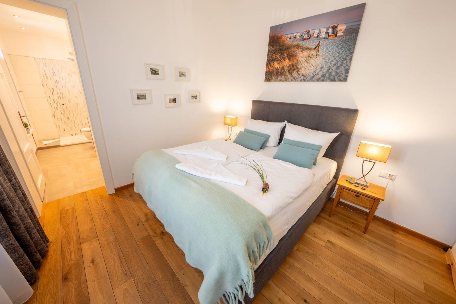 Schlafzimmer mit Bett, Nachttisch und Wandbild. Durchgang zur Badewanne.