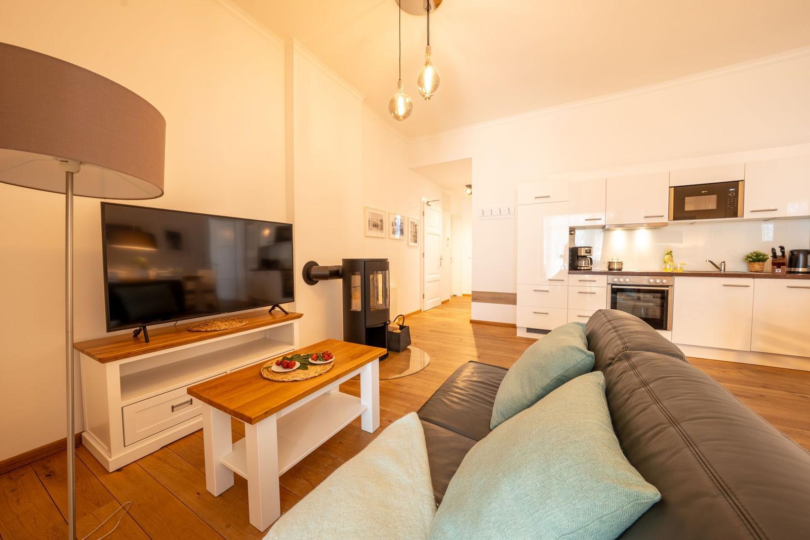 Wohnbereich mit Sofa, Fernseher und Küchenbereich im Hintergrund.
