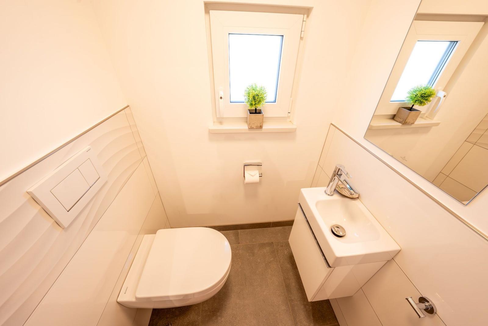 Badezimmer mit Toilette, Waschbecken und Fenster mit Pflanze.