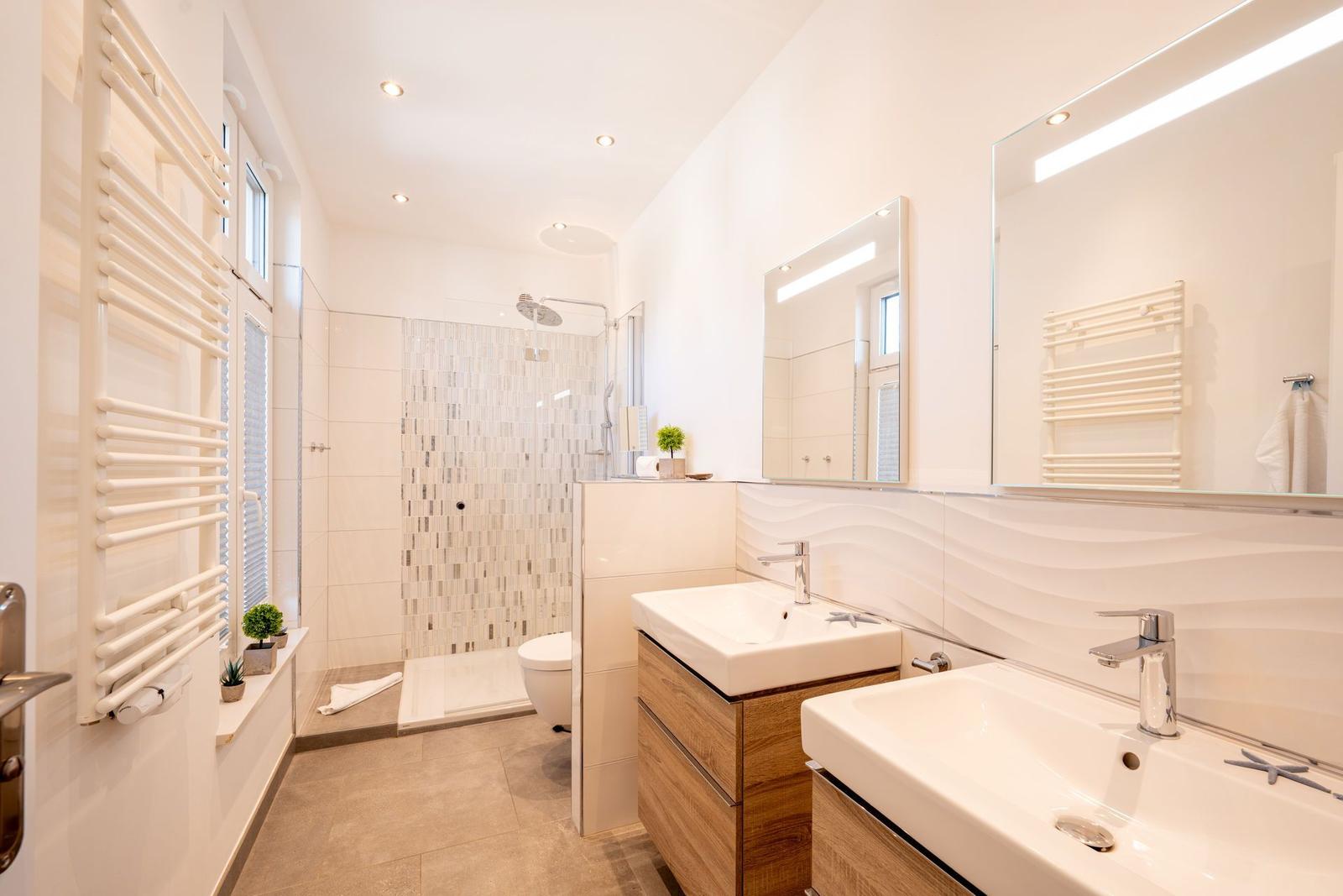 Badezimmer mit Dusche, zwei Waschbecken und Heizkörper