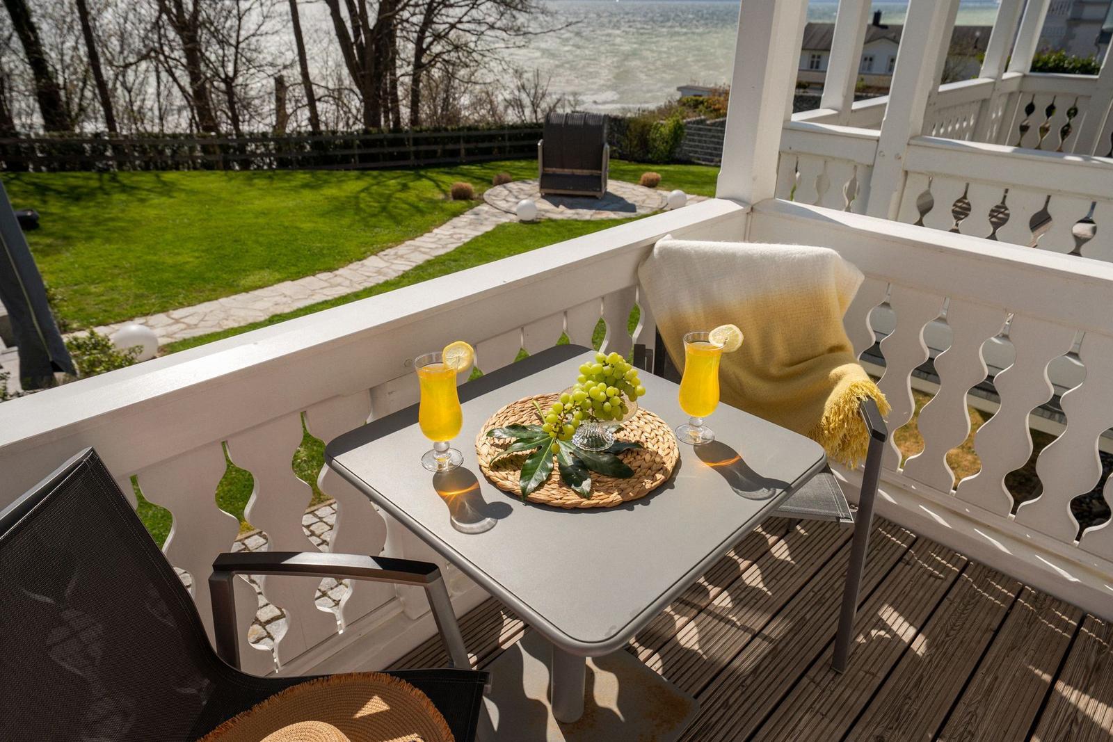 Terrasse mit Tisch, zwei Gläsern und Trauben. Blick auf Garten und Wasser.