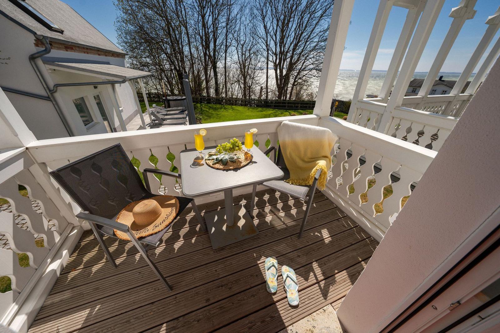 Terrasse mit Tisch, zwei Stühlen und Blick auf Wasser und Grün.