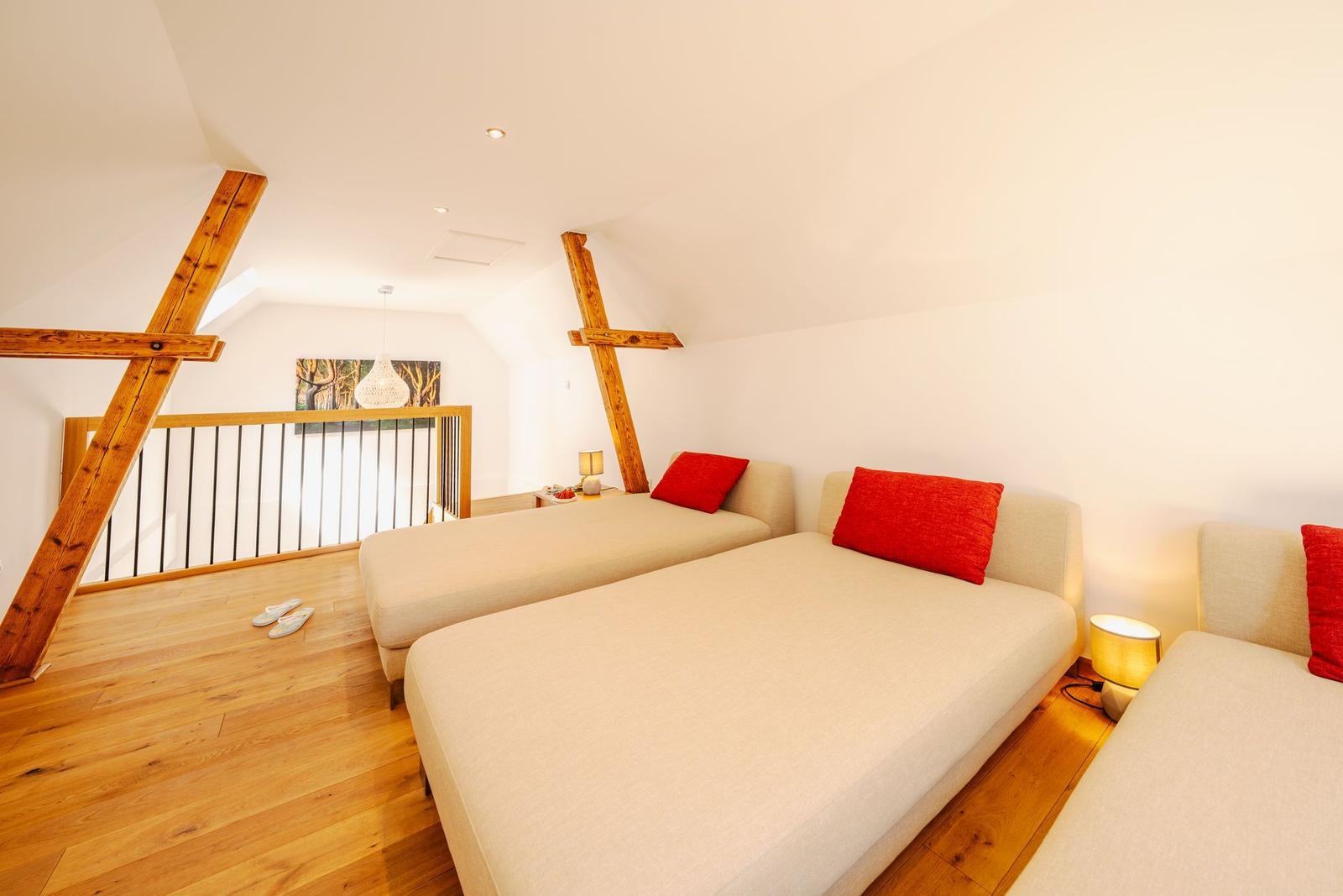 Drei Schlafsofas mit roten Kissen stehen auf Holzdielen unter Holzbalken.