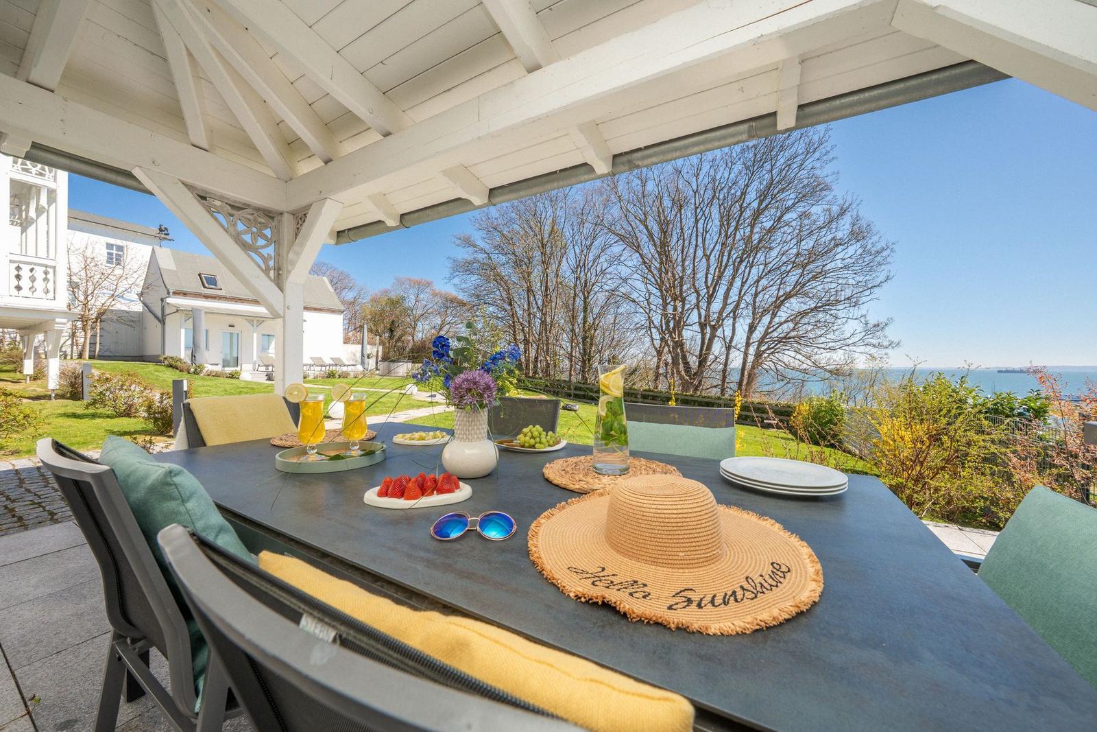 Gedeckter Terrassenbereich mit Tisch, Stühlen und Meerblick.
