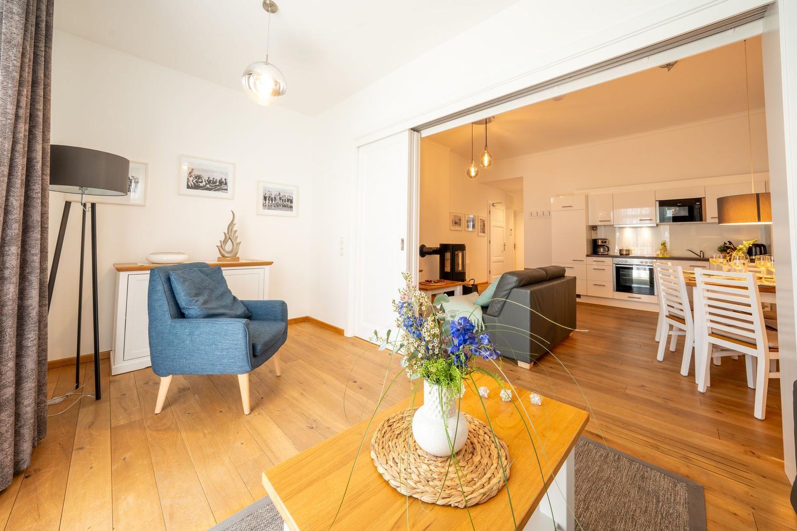 Wohnzimmer mit blauem Sessel und Küche im Hintergrund. Holzboden und modernes Mobiliar.