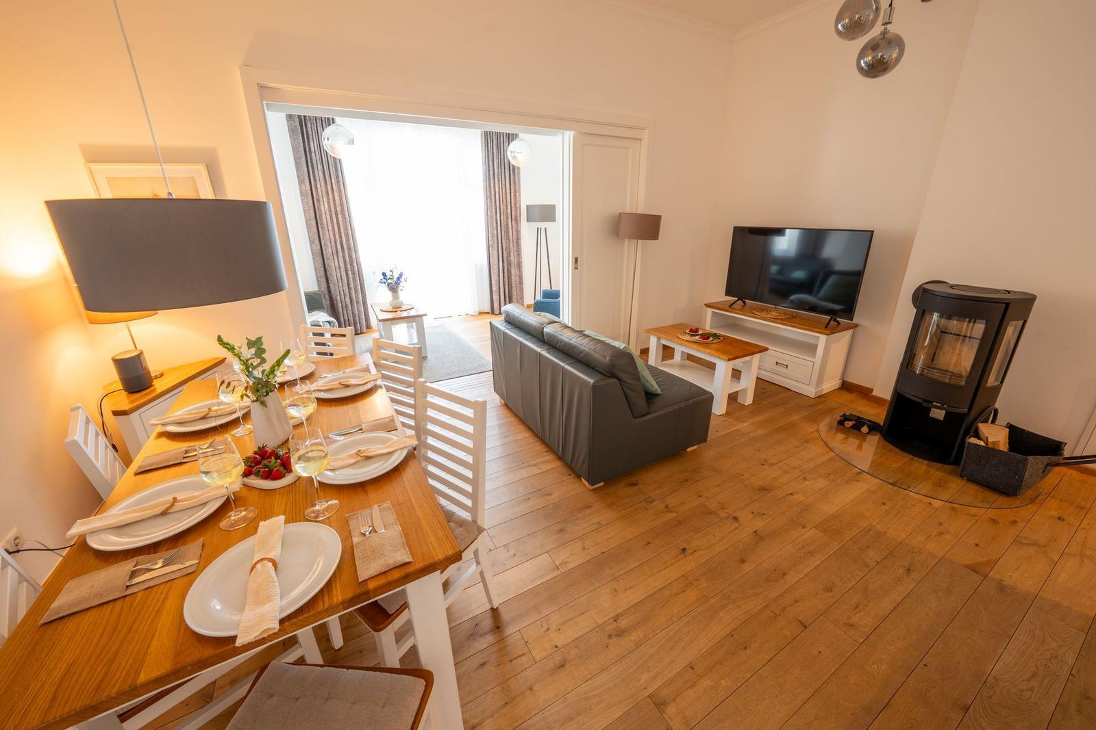 Essbereich mit Tisch und Stühlen. Wohnbereich mit Sofa, Fernseher und Kaminofen.