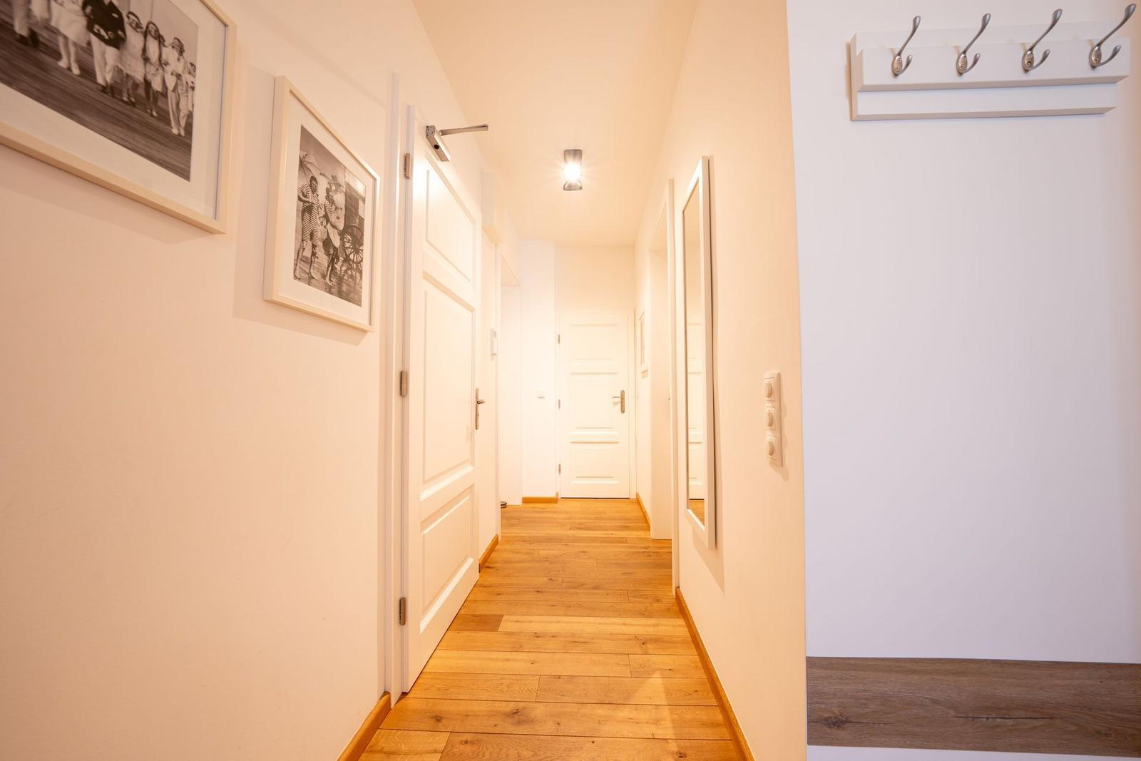 Flur mit Holzboden, weißen Türen und Bildern an der Wand. An der rechten Wand hängt ein Hakenbrett.