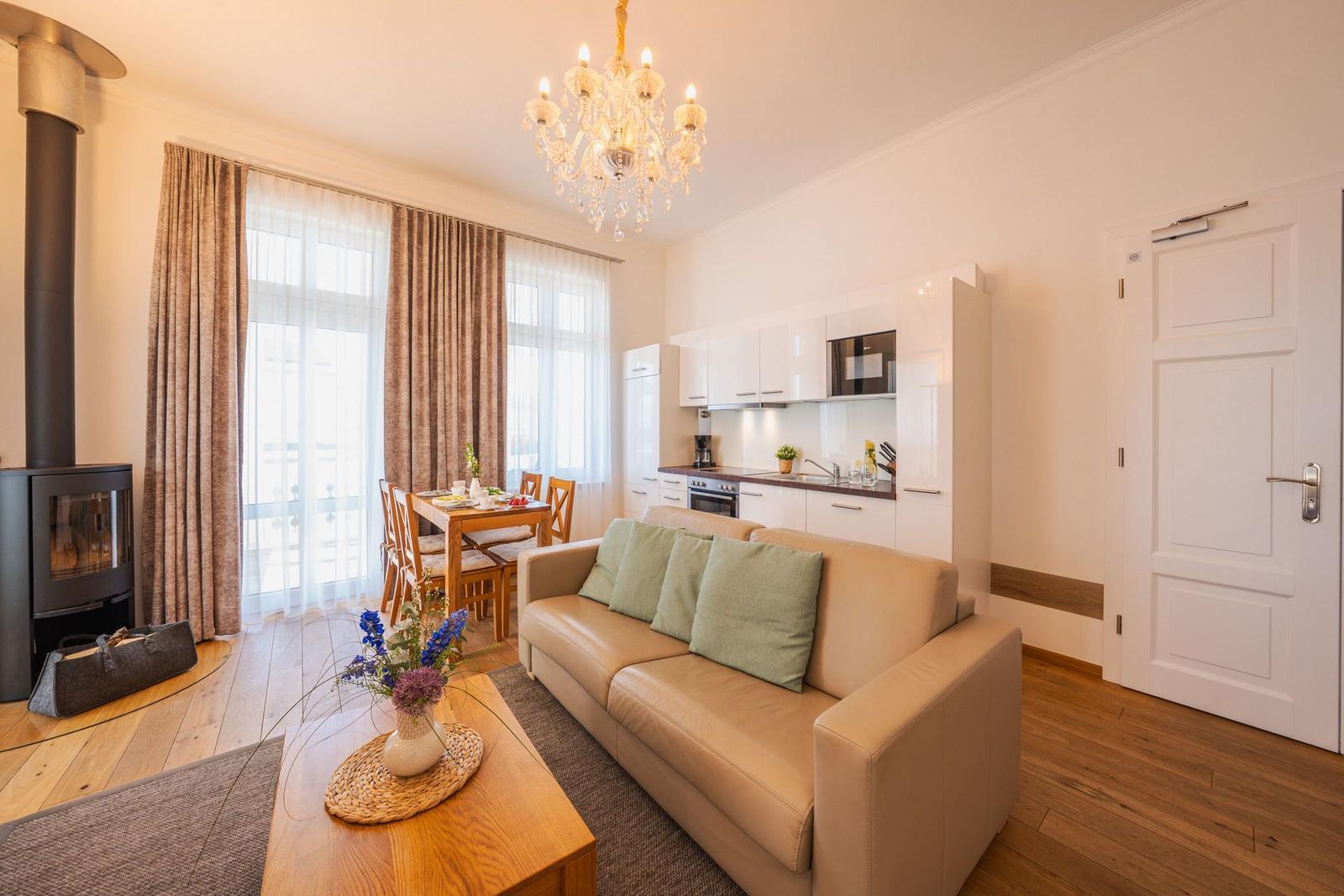 Wohnbereich mit Sofa, Esstisch, Küche und Kaminofen. Holzboden und große Fenster.