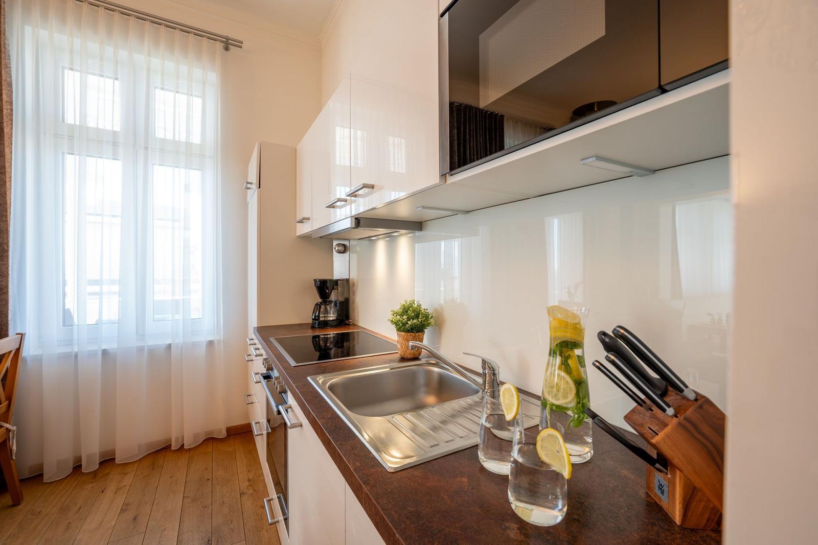 Küche mit Arbeitsplatte, Spüle und Fenster mit weißen Vorhängen.